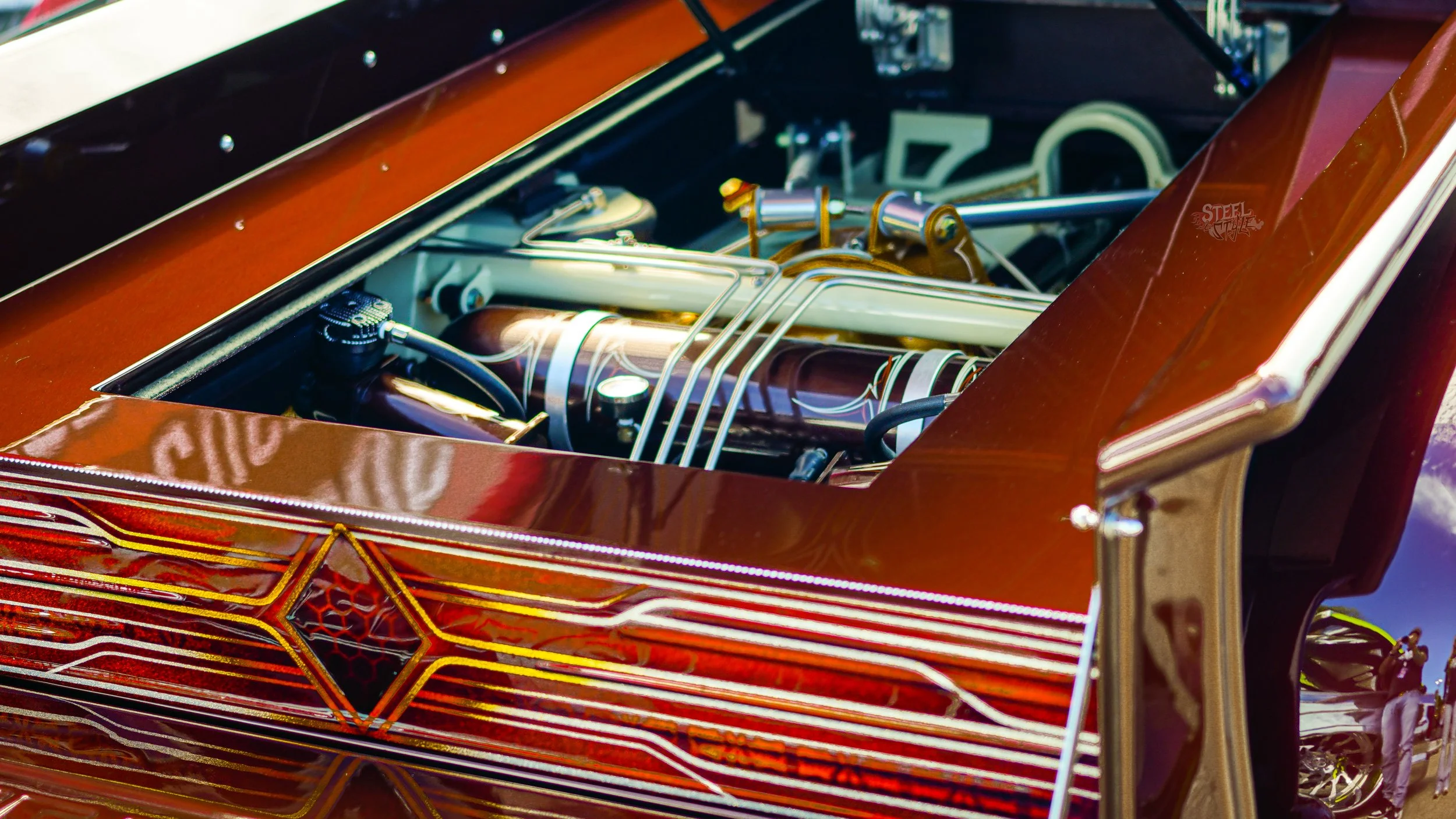 Close-up of a custom, futuristic car engine and intricate paint design on the hood, with reflections of its surroundings.