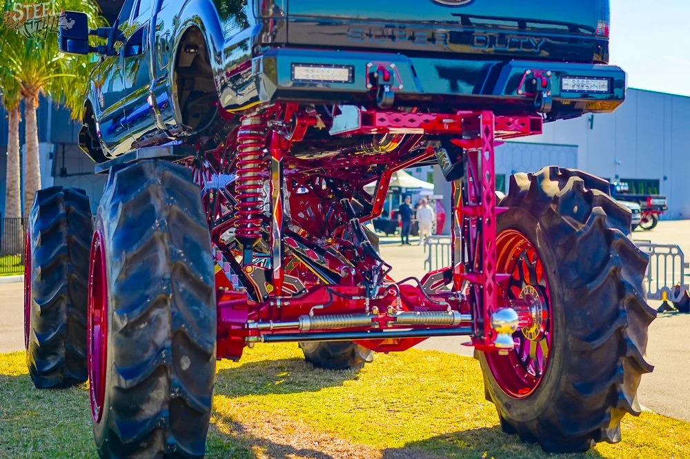 A large modified monster truck with oversized tires, painted in bright colors, on display outdoors at an event.