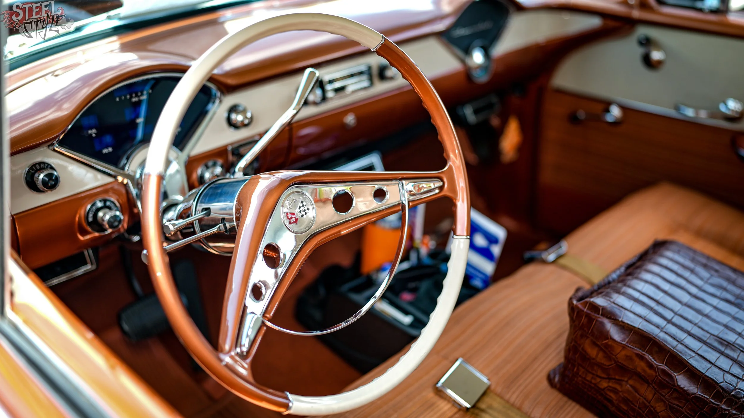 Close-up view of the interior of a vintage car, featuring a tan and cream steering wheel, a wooden dashboard, and a brown leather seat.