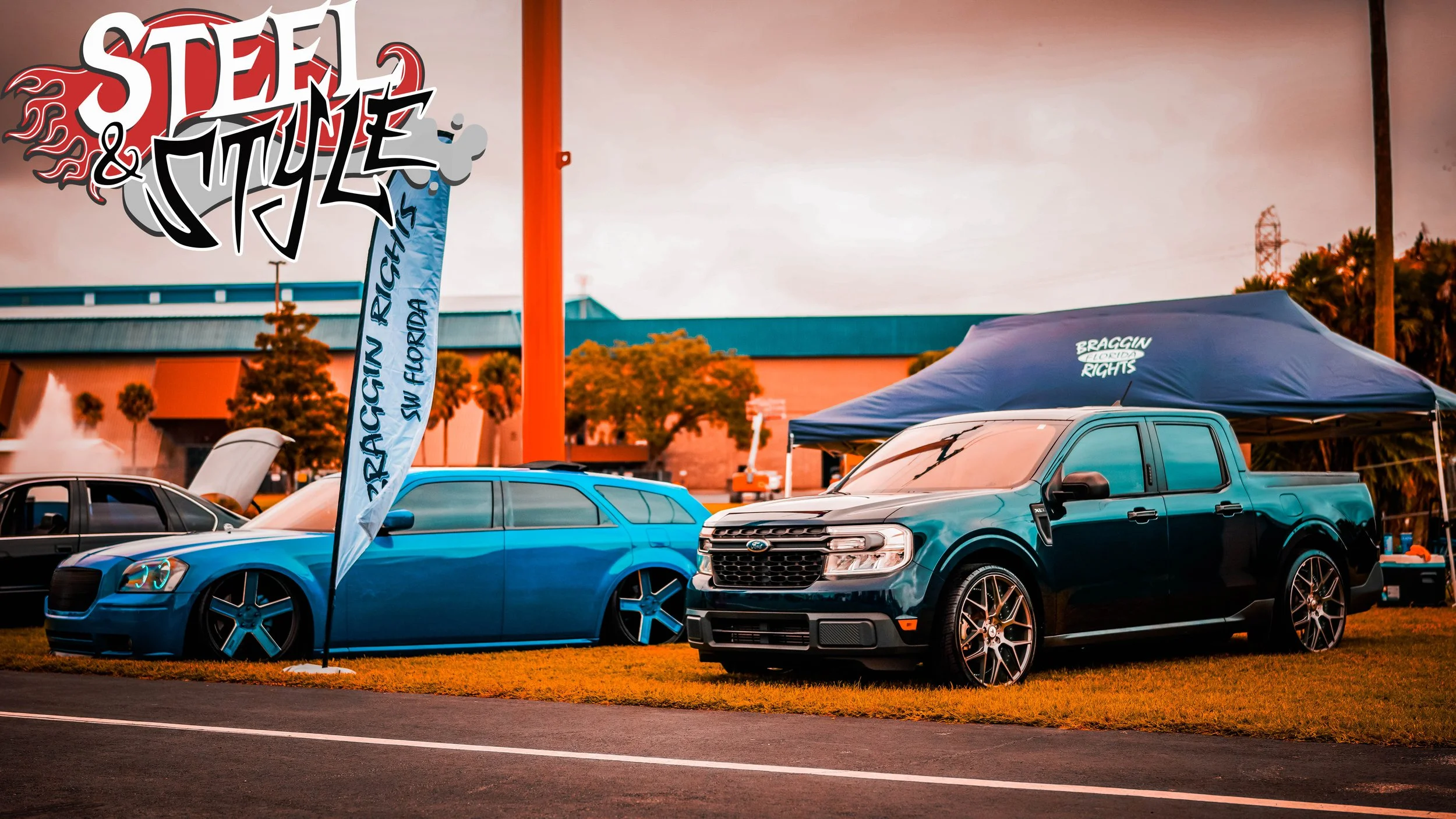 A blue painted Ford vehicle and a black super crew pickup truck parked on a grassy area at an outdoor event, with a tent in the background and a banner that reads 'RACIN RIGHS SW FLORIDA', 'STEE & MYLE' and a stylized logo.