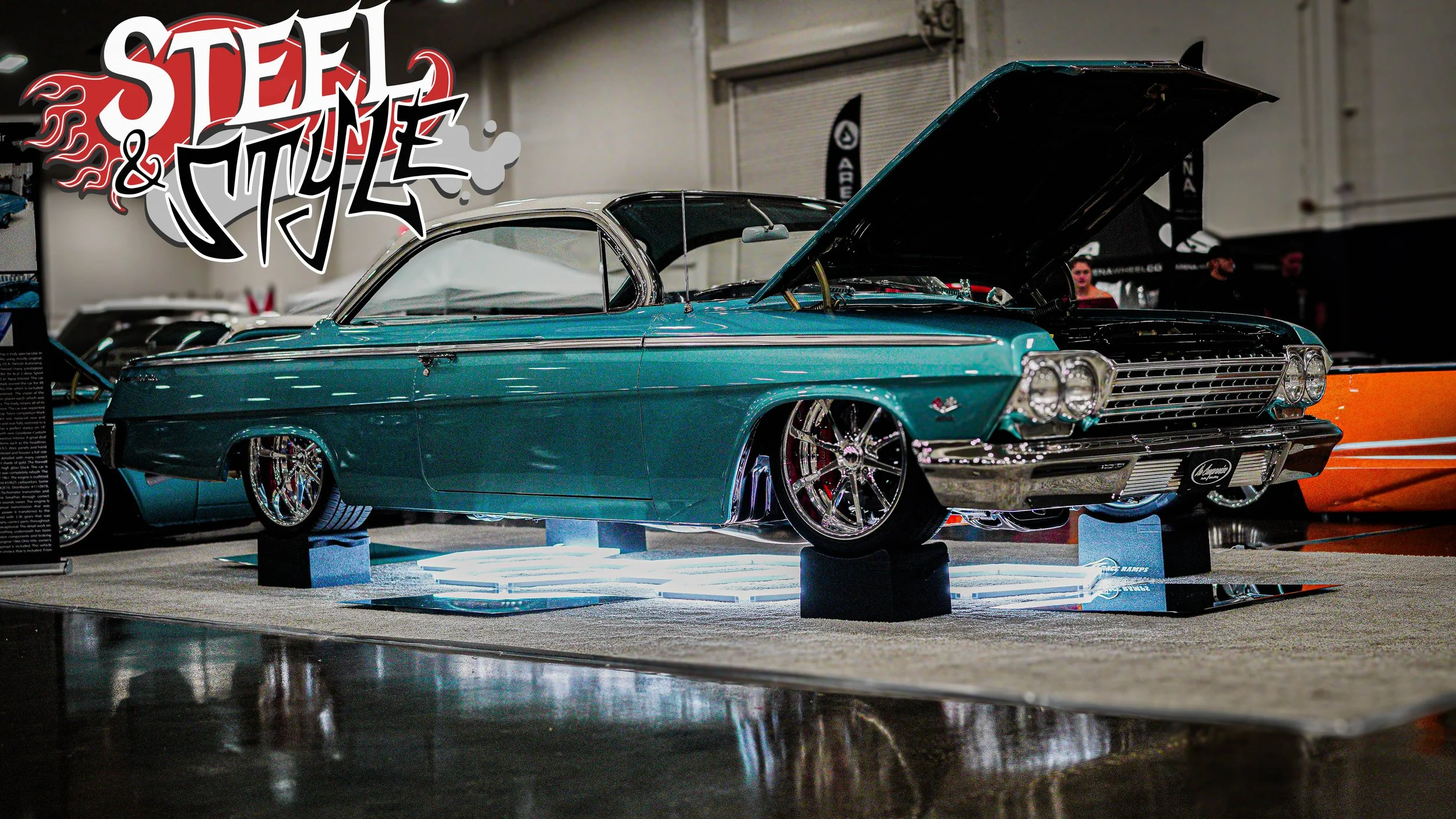 A vintage teal Chevrolet car with its hood open, displayed at an indoor car show, with a 