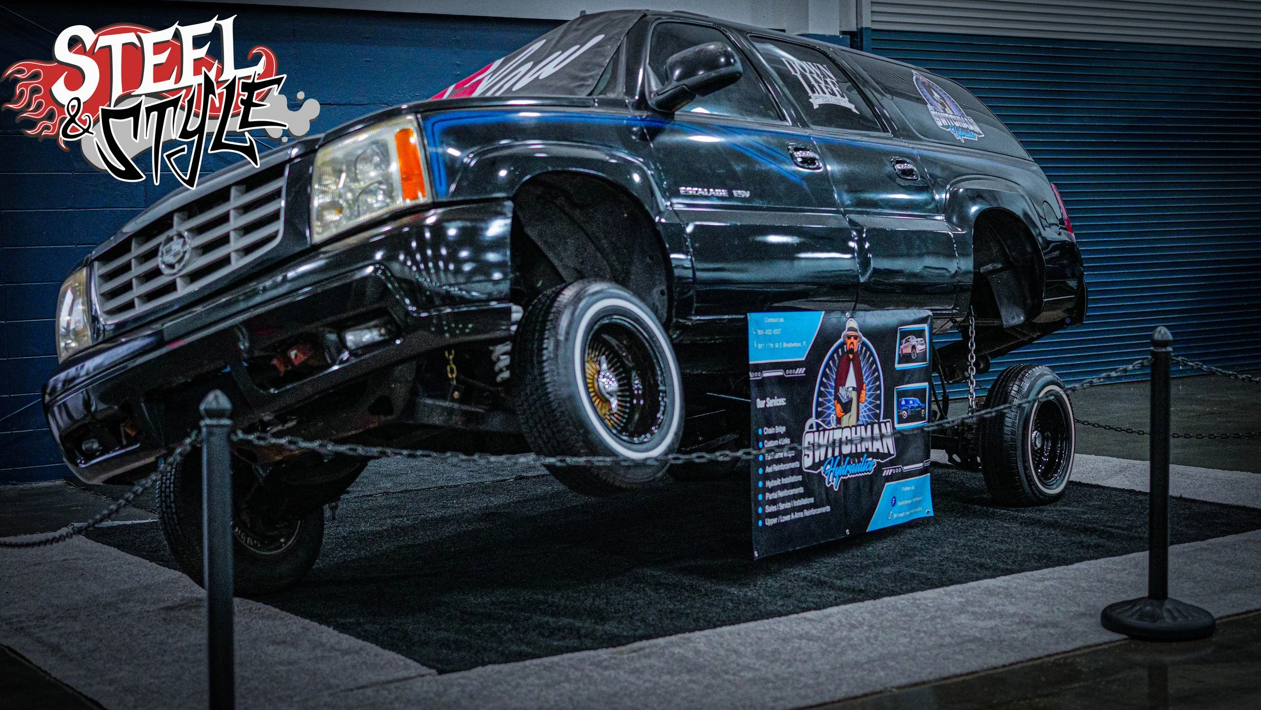 A black vintage car displayed on a stand at an exhibition with a sign in front and a logo that says 'Steel & Style' on the top left corner.