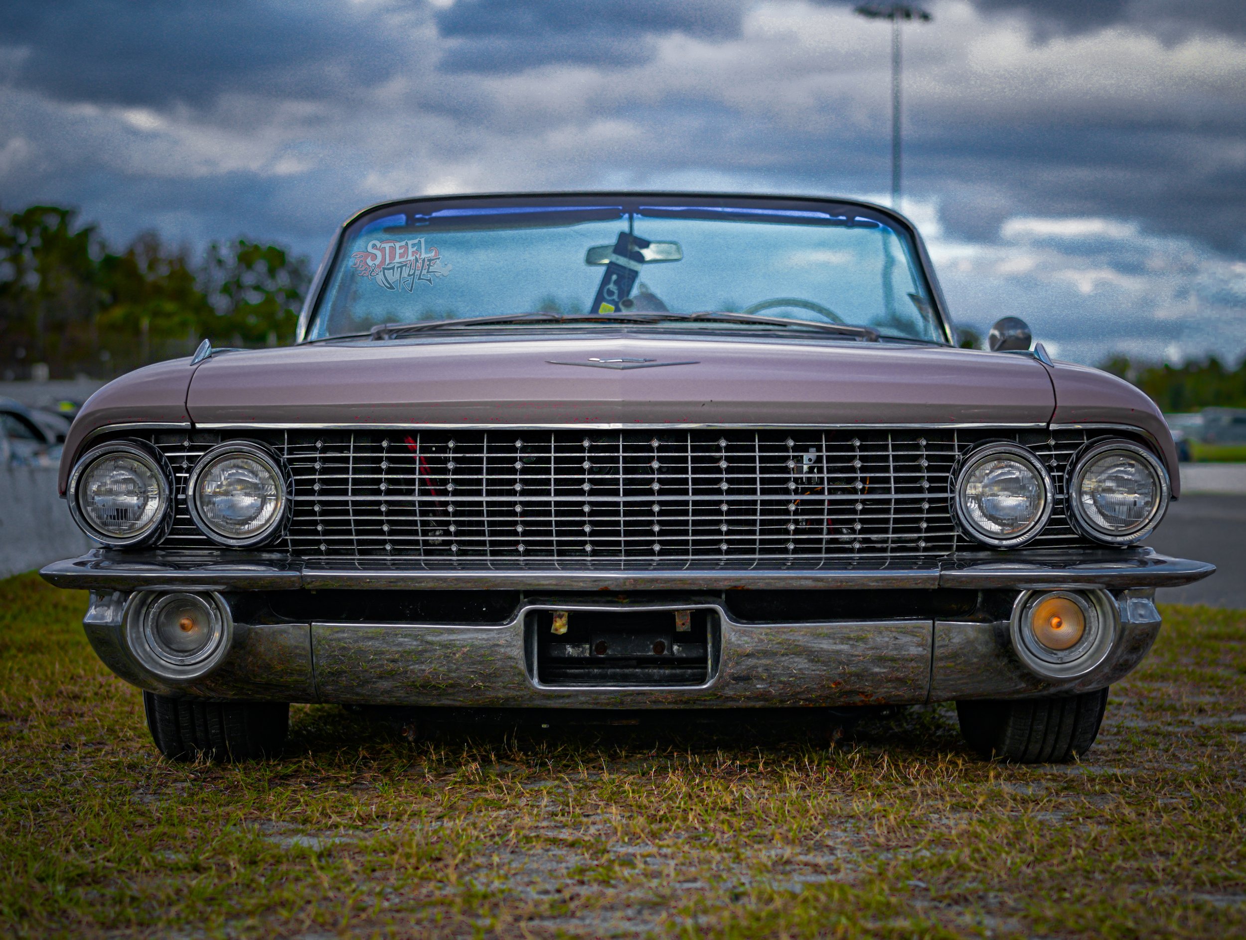Front view of a vintage gray convertible car parked on grass, with a cloudy sky in the background.