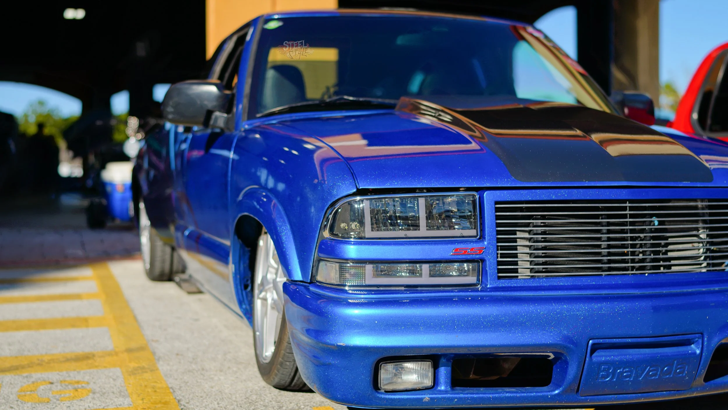 A blue Chevrolet Camaro with custom black racing stripes on the hood, parked in a parking lot.
