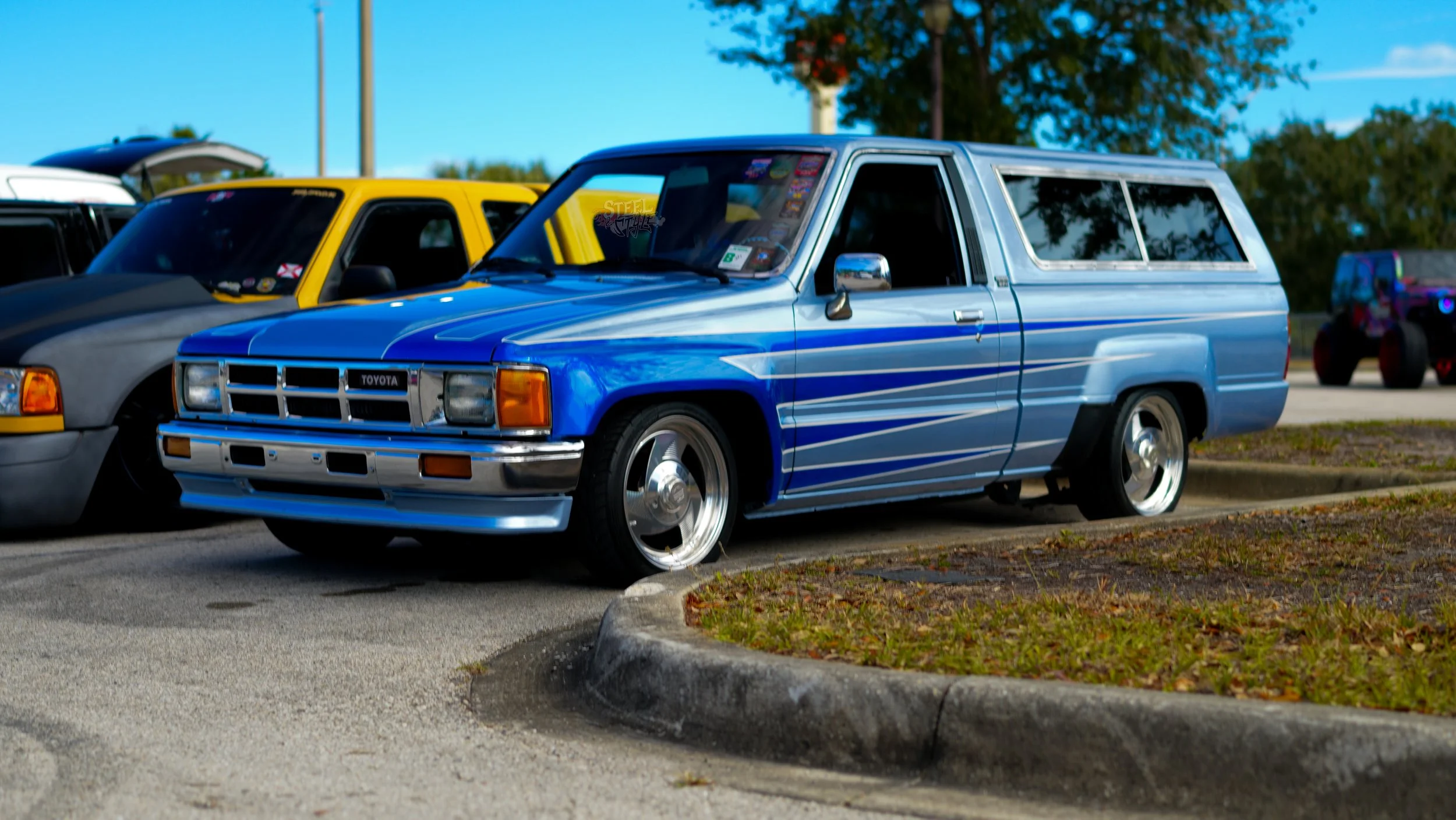 A vintage blue Toyota SUV parked in a parking lot next to other cars under a clear blue sky.