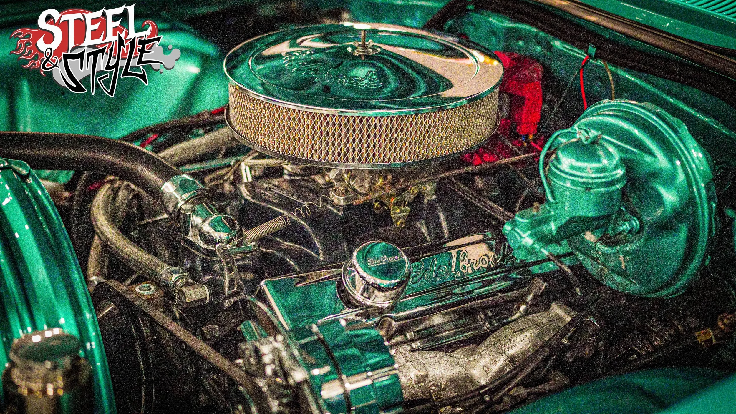 Vintage car engine with chrome components, a large round air filter, and custom green paint, labeled Edelbrock, with a 'Steel & Style' decal in the top left corner.