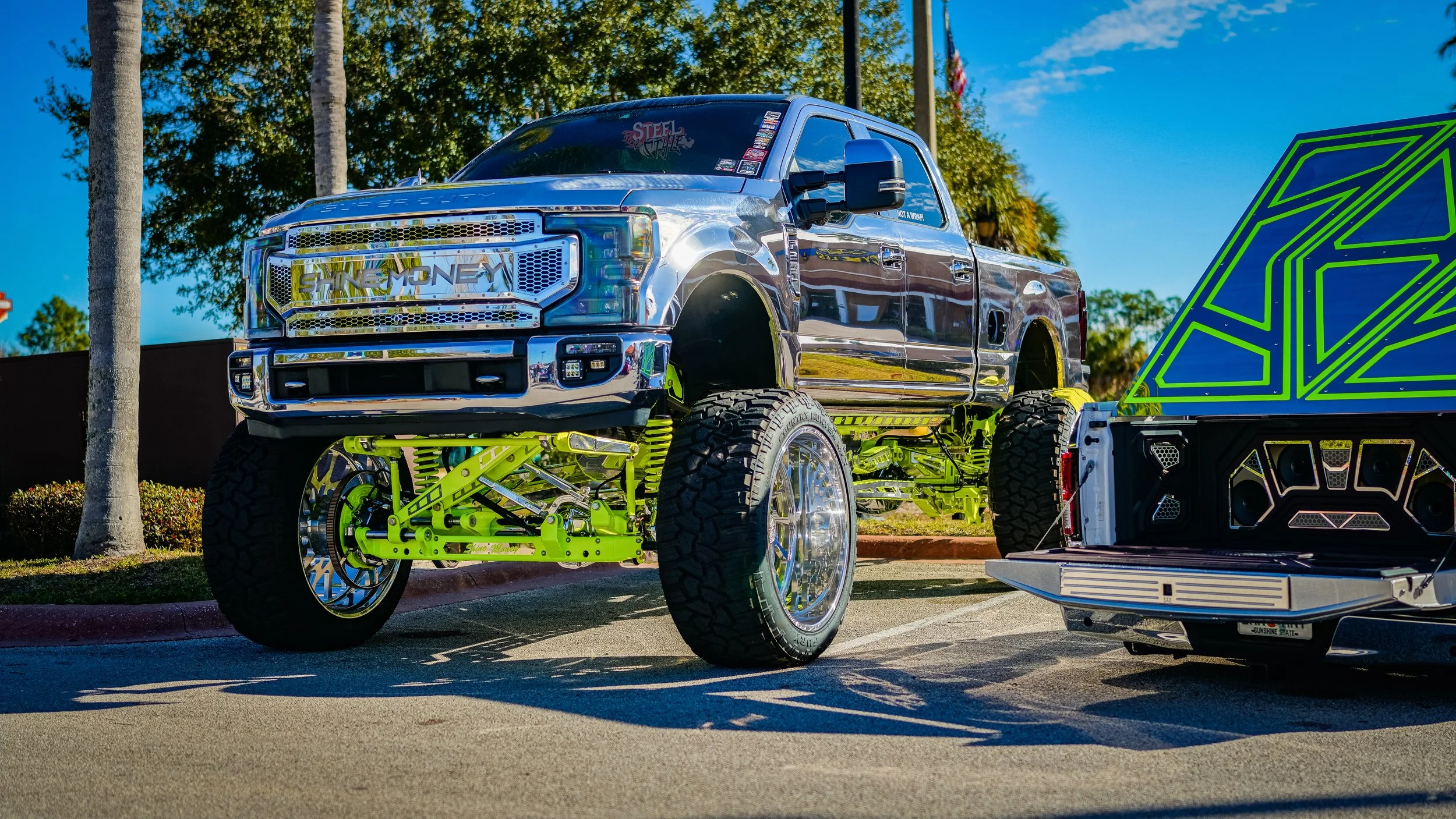 A chrome-plated lifted truck with large tires parked in a lot next to a trailer.