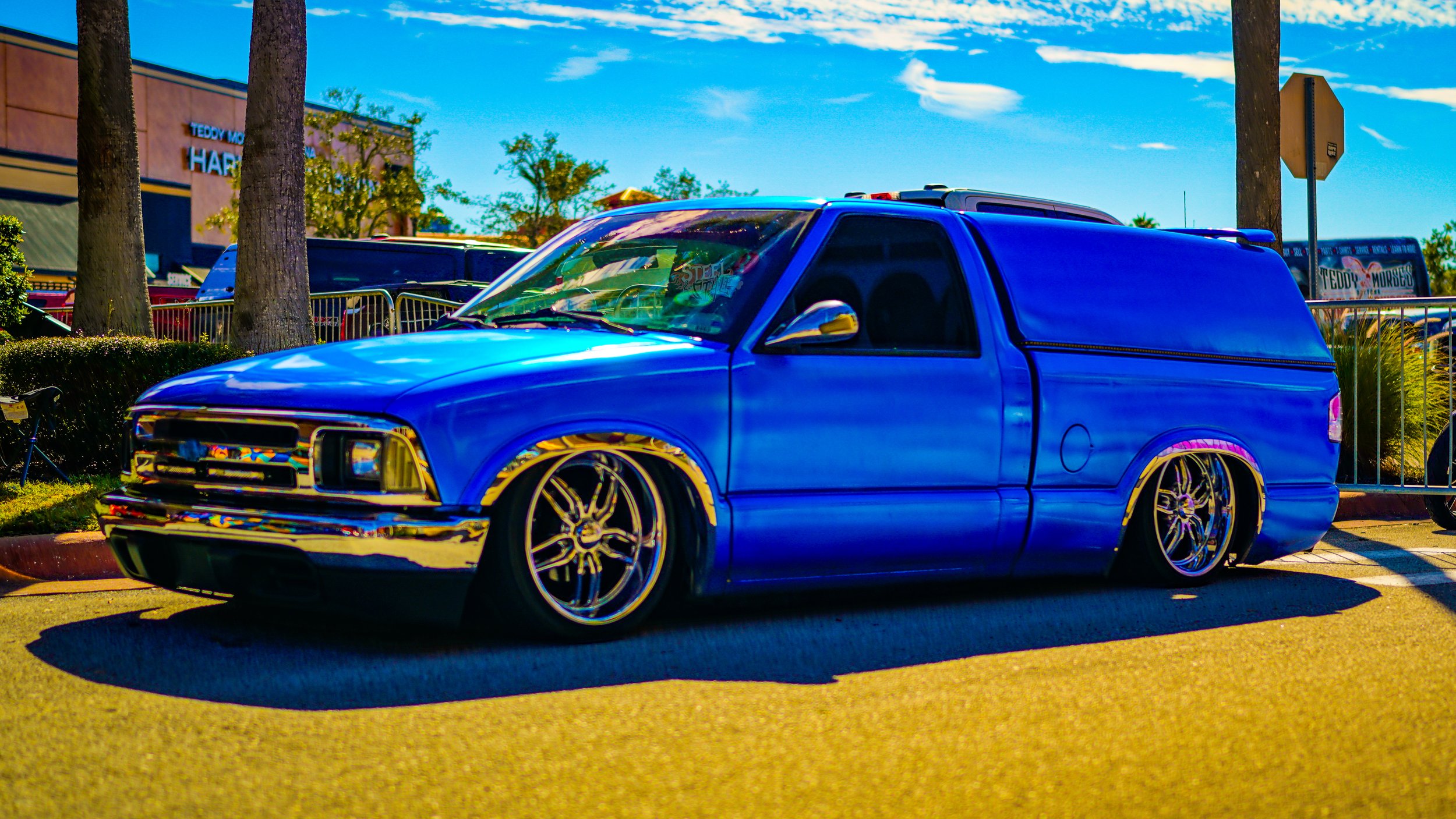 Blue customized van with chrome wheels parked outdoors on sunny day.
