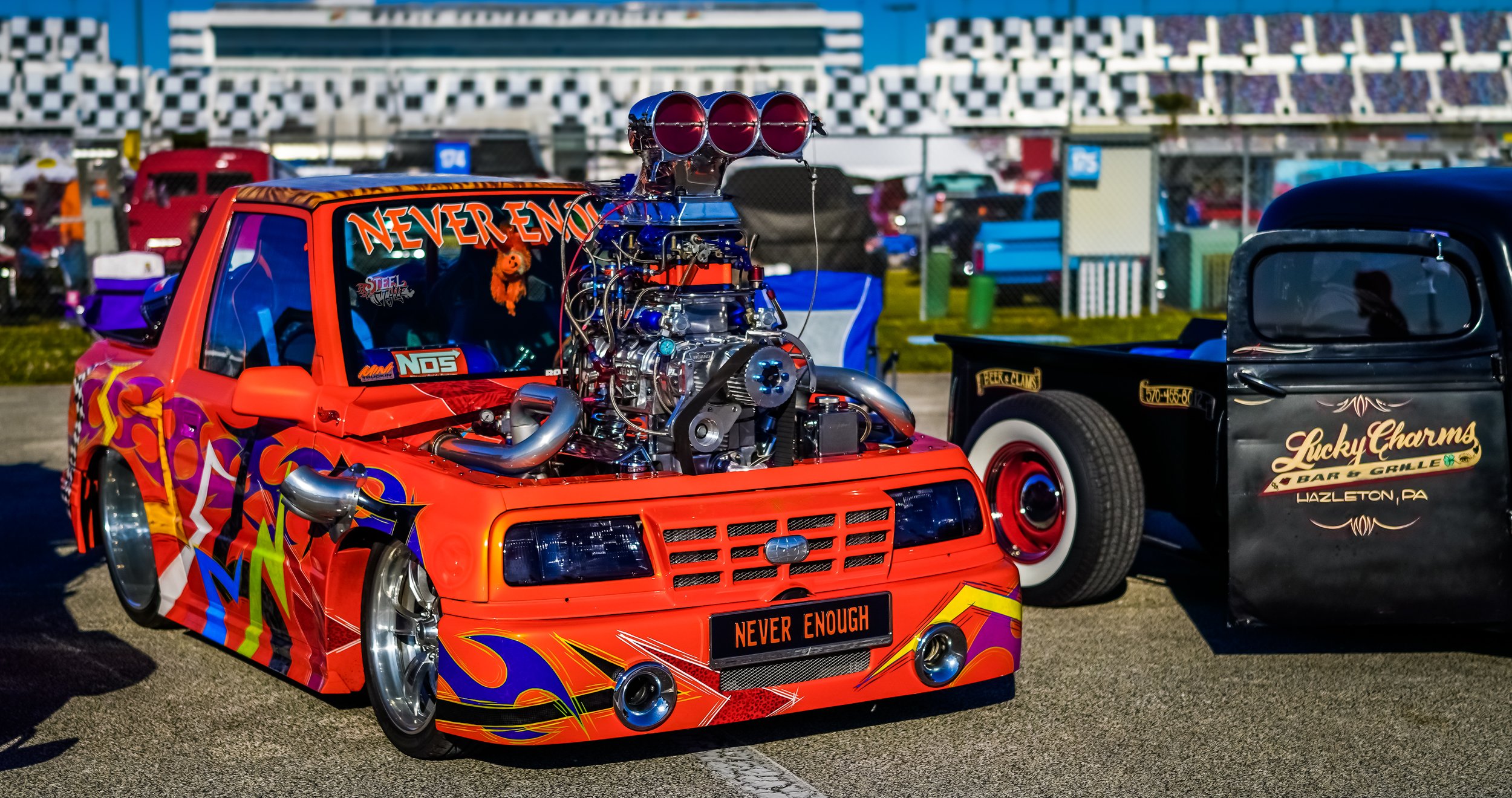 A heavily modified orange race car with a large exposed engine and colorful graphics, displayed at a car show.