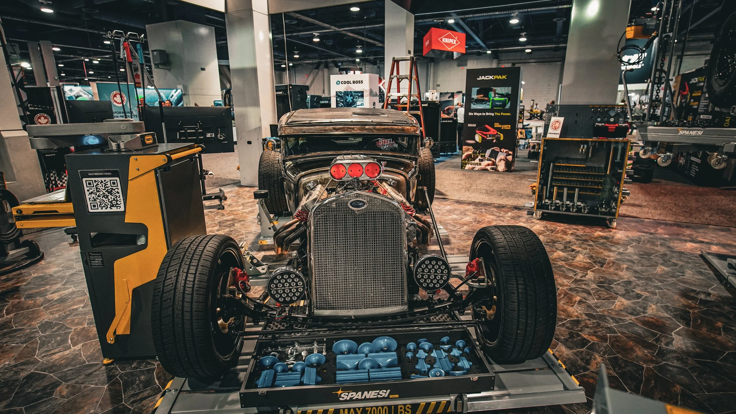 Display of a vintage race car with exposed engine parts in a showroom, surrounded by tools and equipment.