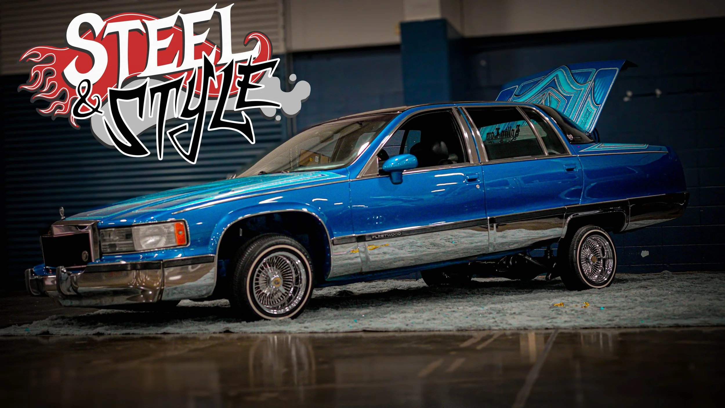 A vintage blue car with a futuristic design in a dimly lit indoor setting, with graffiti-style text 'Steel & Style' in the background.