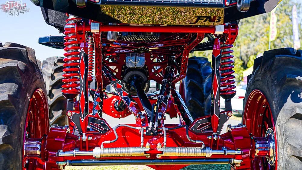 Close-up of the undercarriage of a race car with red suspension components, large tires, and detailed mechanical parts visible.