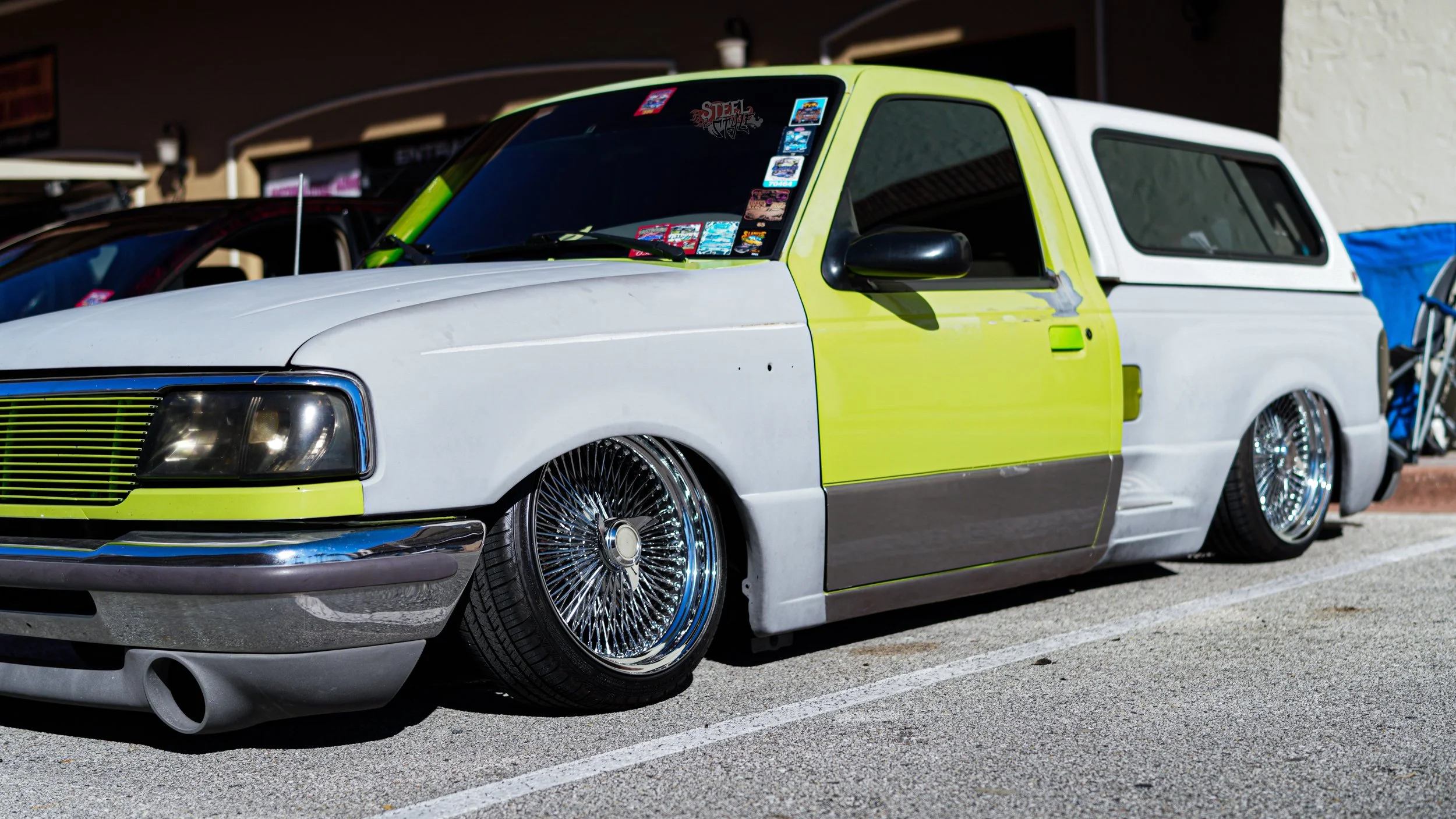 A lowered white and lime green vintage pickup truck with custom wire-spoked wheels parked on street.