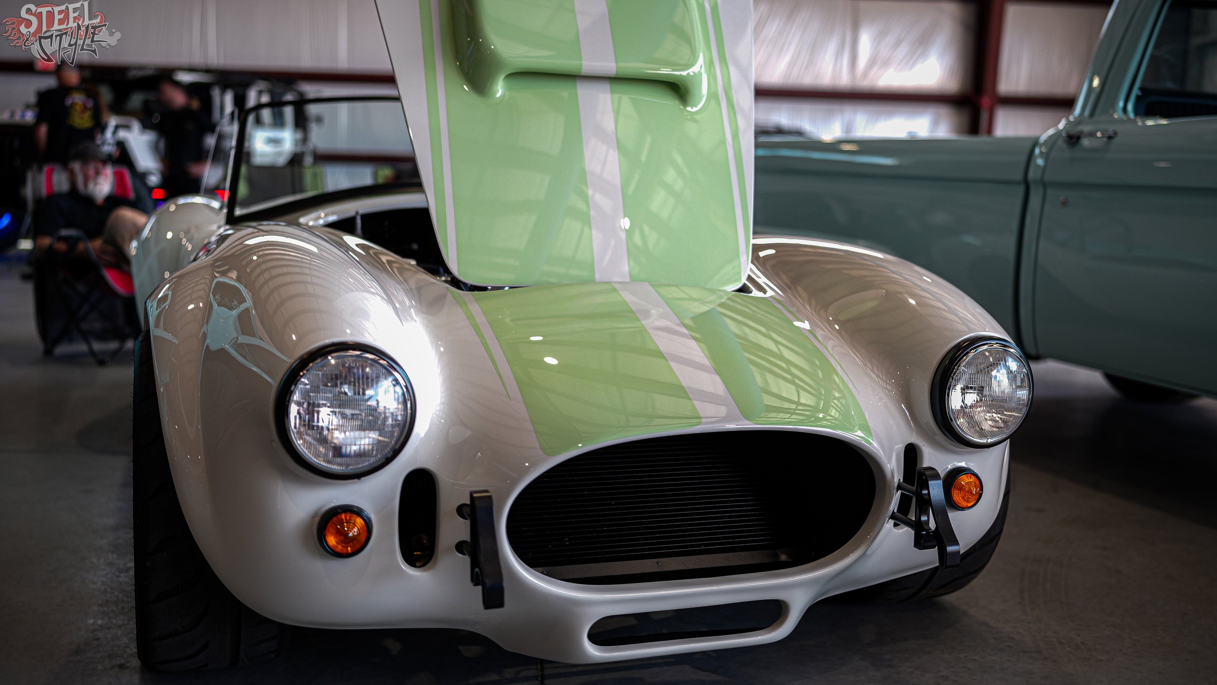 A vintage race car with a silver body and green racing stripes displayed at an indoor car show.