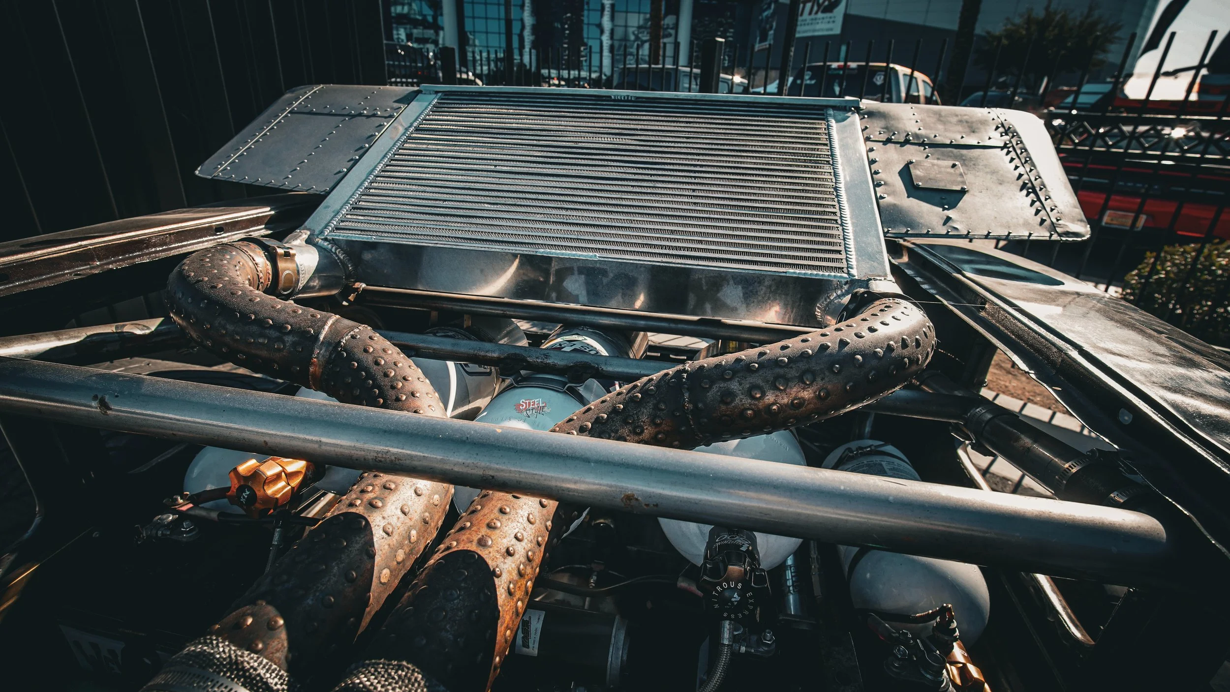 Close-up of a race car engine with a large radiator, heat-exchanging pipes, and various mechanical components.