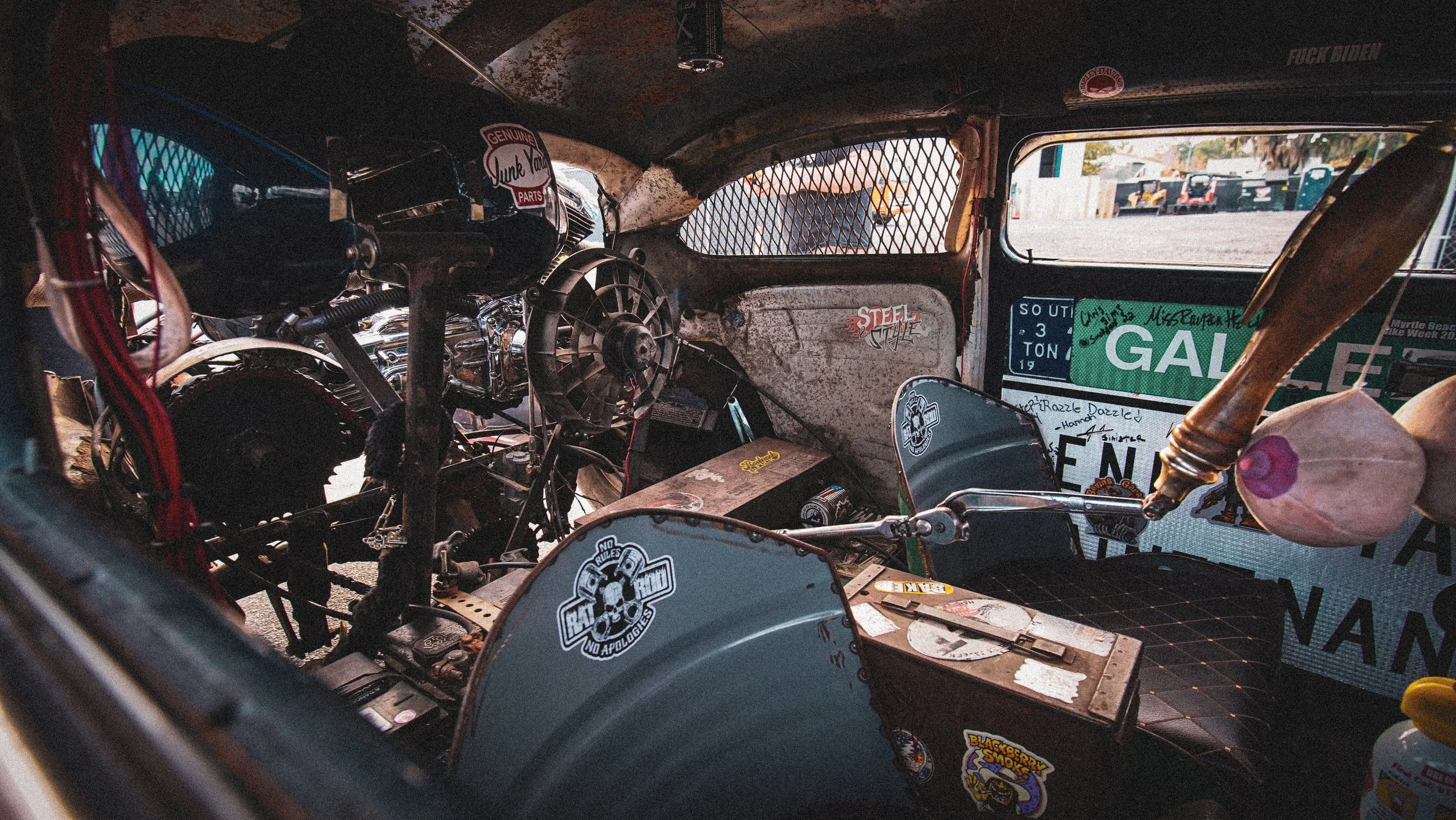 Interior of a vintage race car with visible steel dashboard, racing stickers, and a wooden gear shifter.