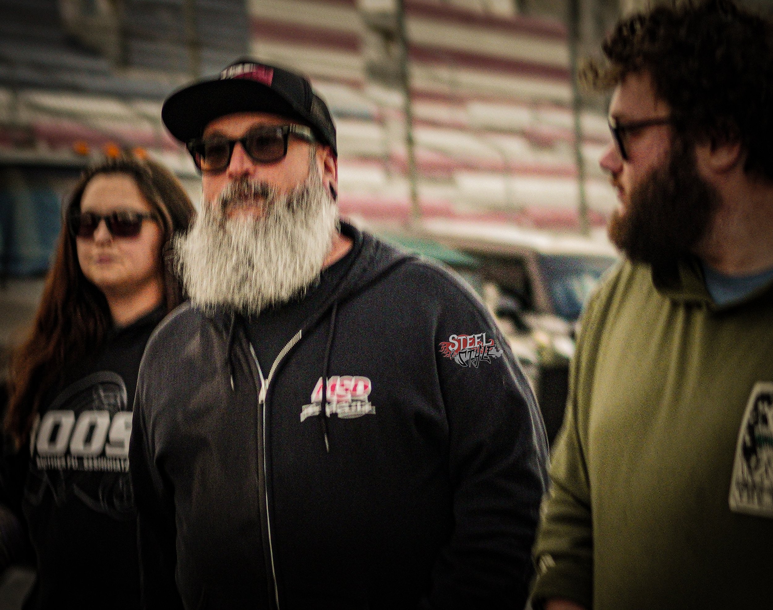 Three people standing together in an indoor setting, wearing sunglasses and casual clothing.
