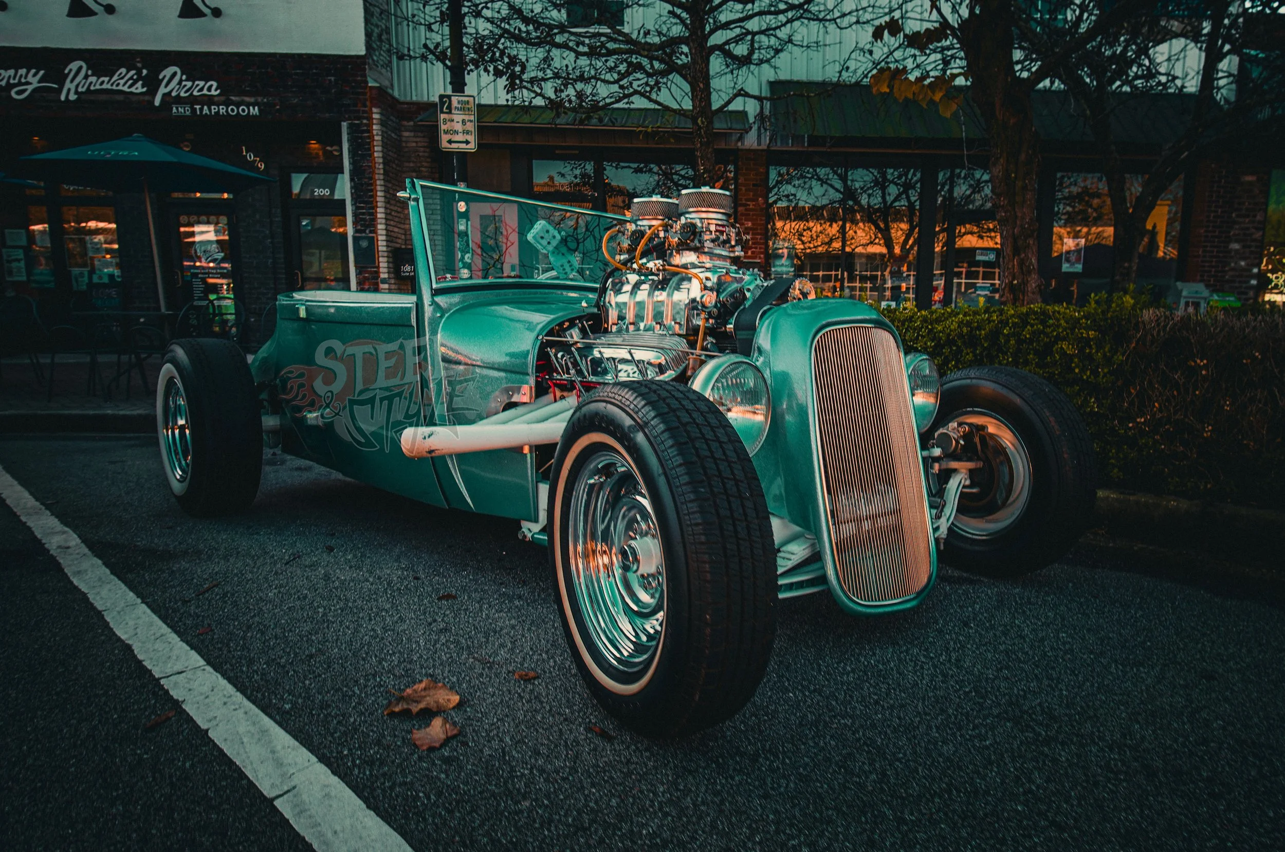 Vintage race car with exposed engine parked outside a restaurant at sunset.