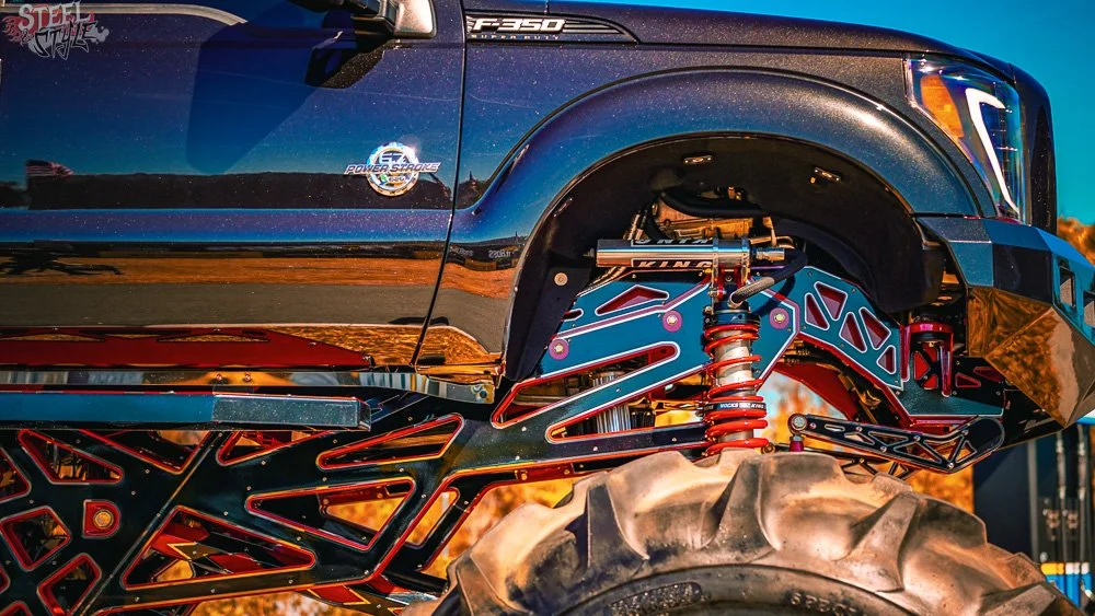 Close-up of a black off-road monster truck with large tires, exposed suspension system, and intricate red and black framework.