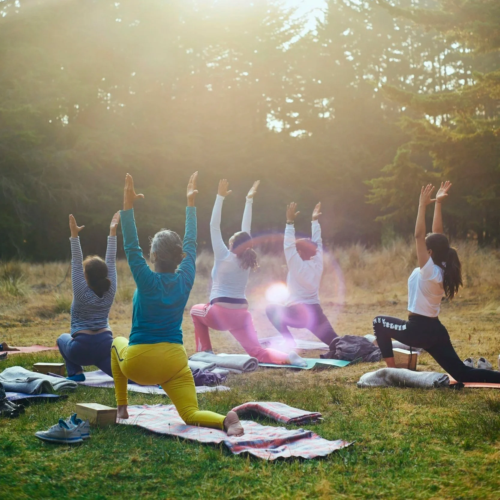 Group of women practicing yoga outdoors in a field during sunrise or sunset.