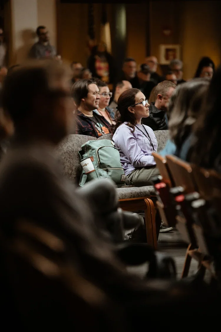 Audience members seated in a dimly lit auditorium attentively listening to a presentation or speaker.