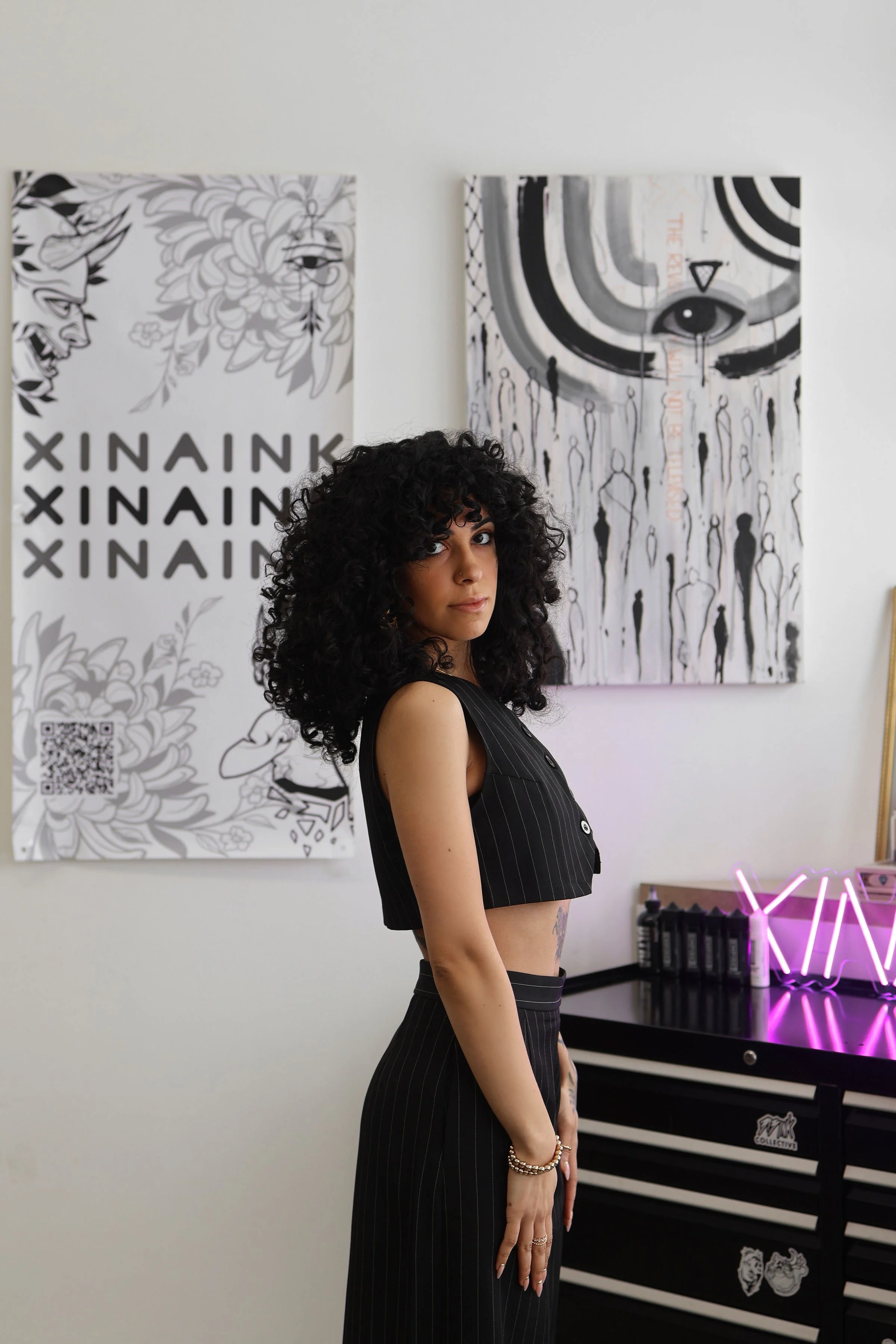 Rowaida, tattoo artist and owner of XinaInk in Detroit, standing in her studio surrounded by her artwork