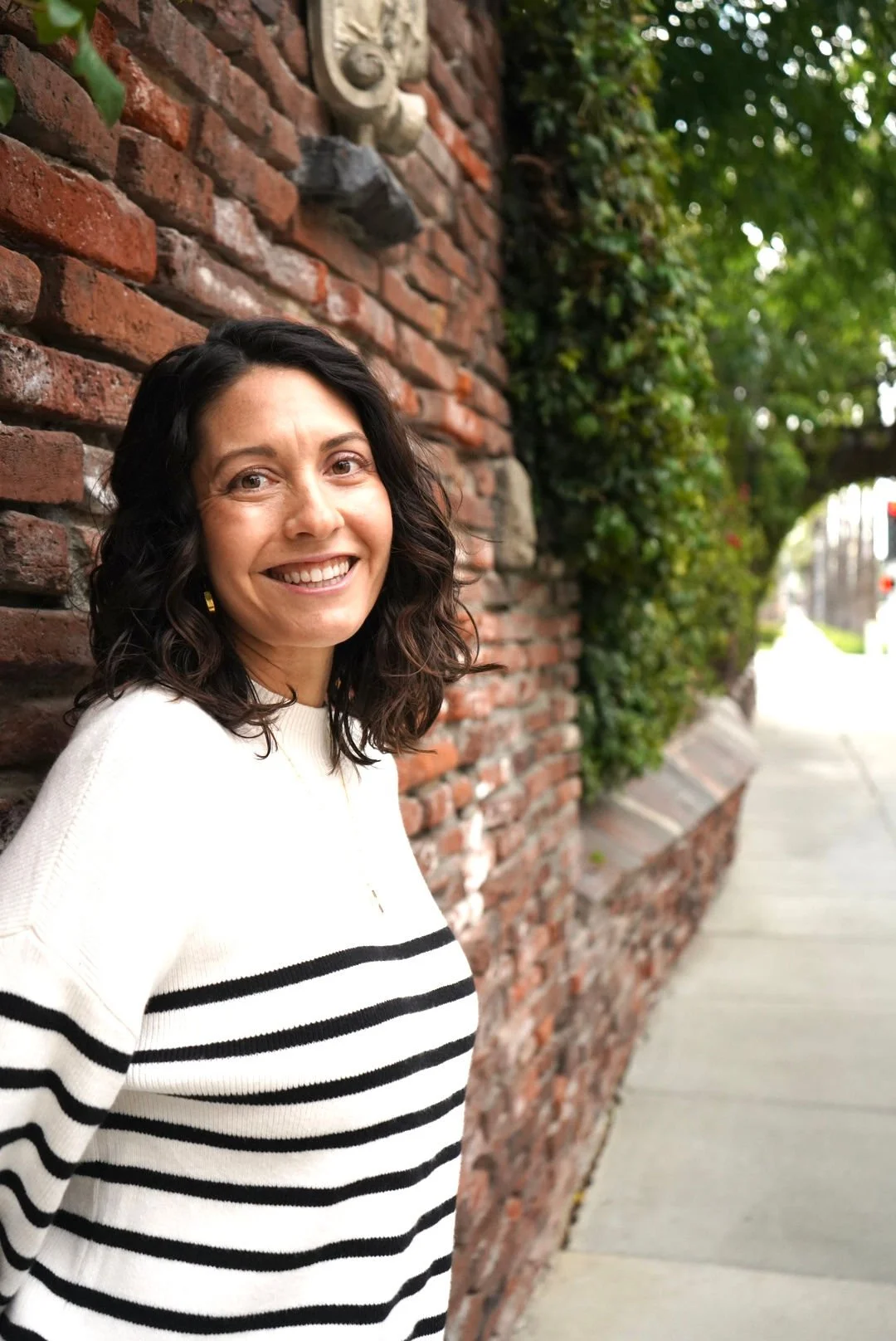 woman with brown hair leaning next to a brick wall