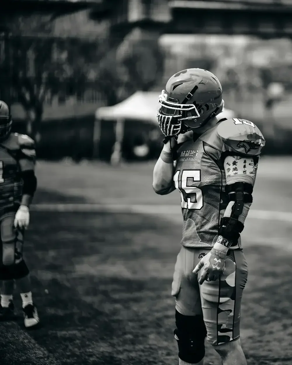 A football player in full gear, including a helmet, gloves, and padded uniform, standing on a field with a blurred background.