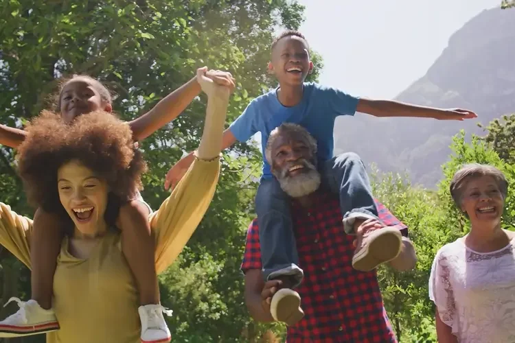A diverse group of happy people outdoors, including children and adults, enjoying a sunny day in nature.