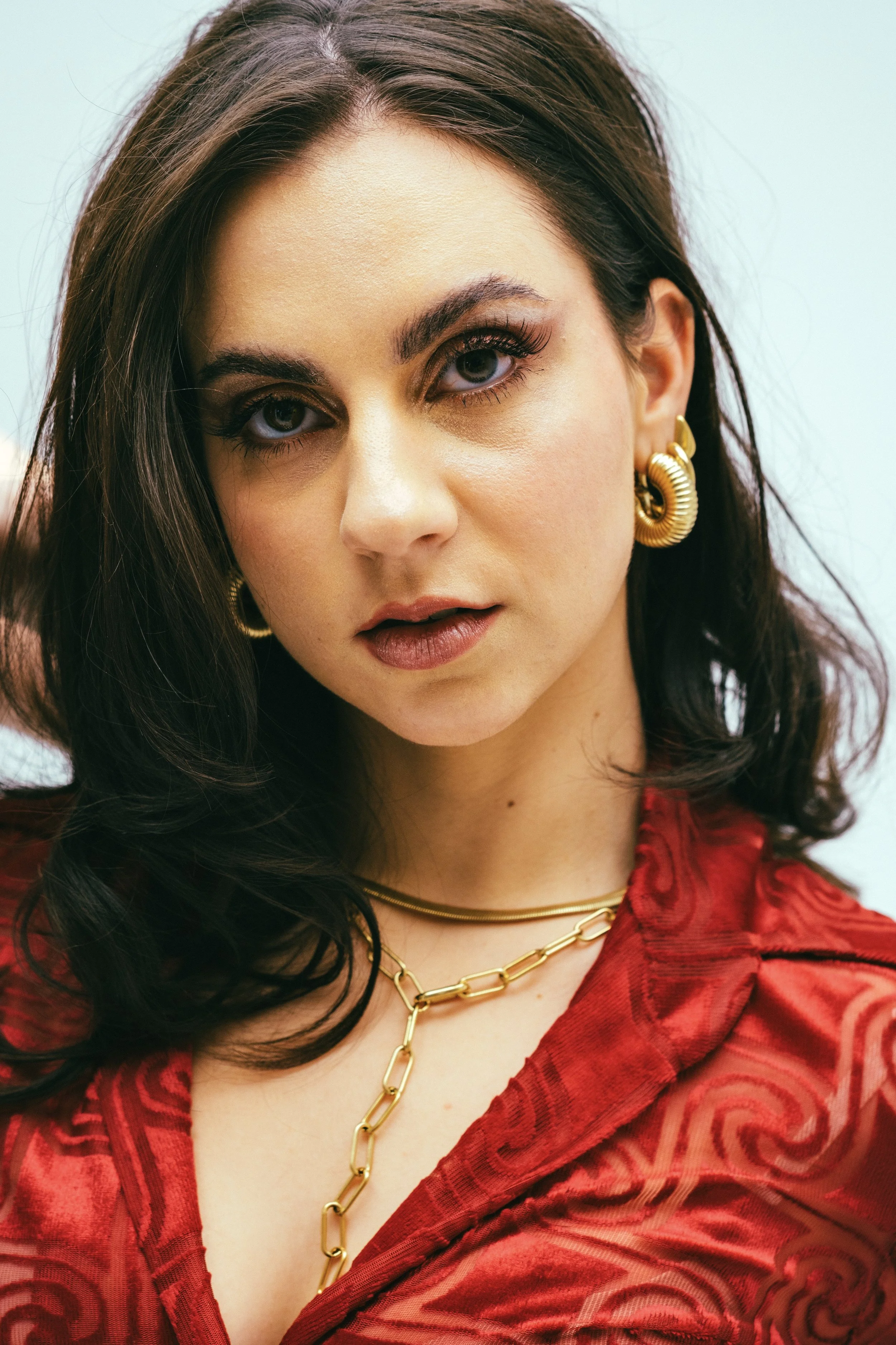 Nahaufnahme einer jungen Frau mit dunklem Haar, goldener Schmuck und rotem Kleid.