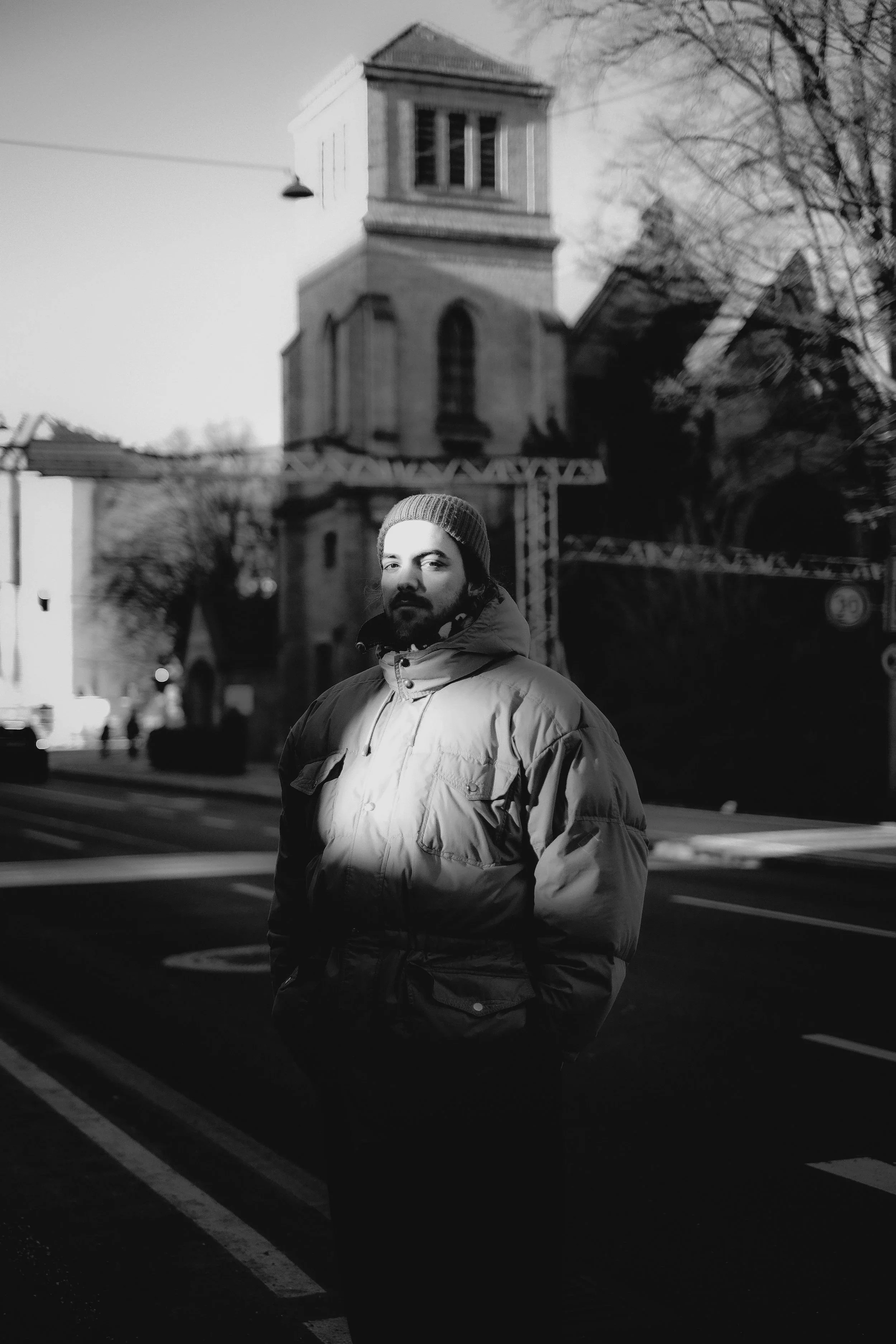 Ein Mann in warmem Mantel und Mütze steht nachts vor einer historischen Kirche auf einer Stadtstraße, beleuchtet vom Straßenlaternen.