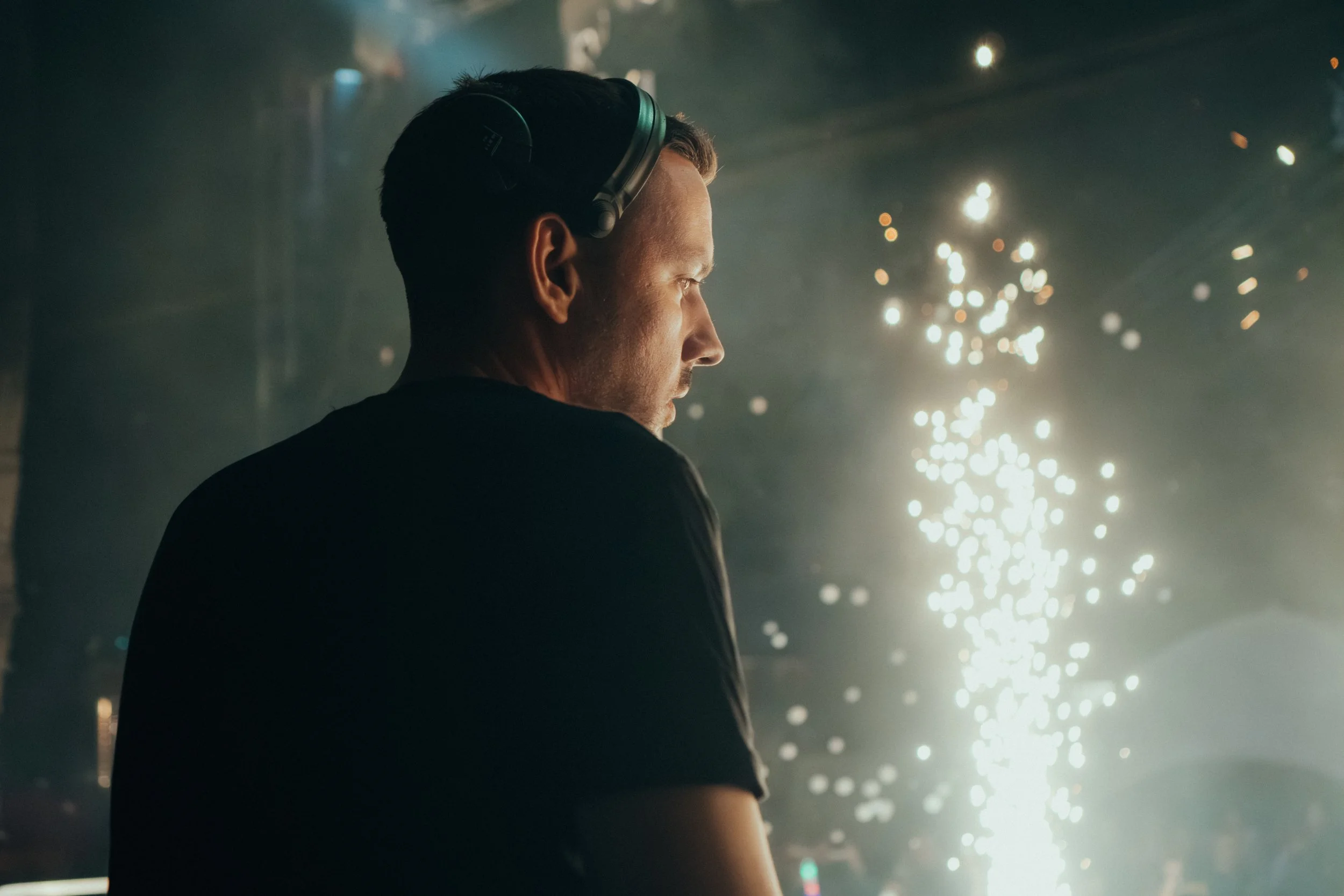 Mann mit Kopfhörern, im Profil, bei einer Feier mit Funken im Hintergrund.