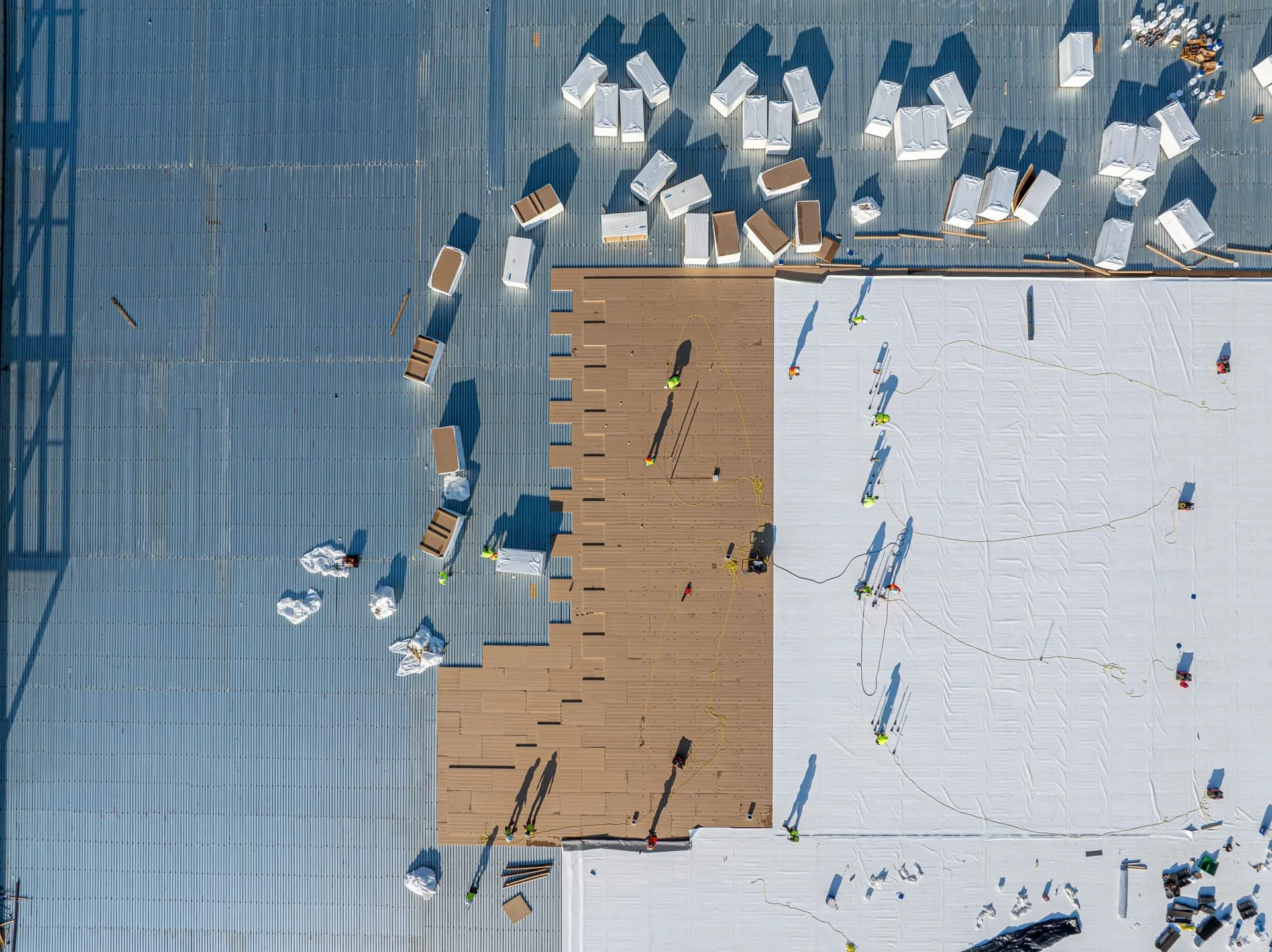 Drone aerial photo of construction workers installing metal roof insulation panels on a commercial building in Cedar Park, Texas.