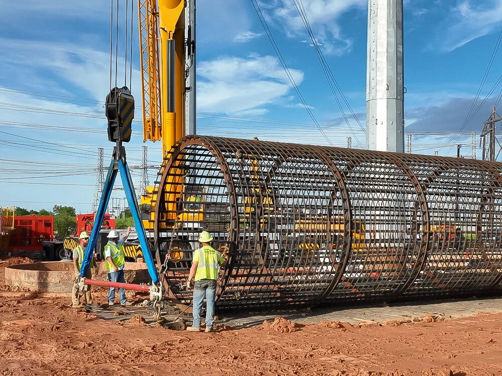 Construction crew guiding cylindrical rebar cage with crane at utility infrastructure progress photography for contractors