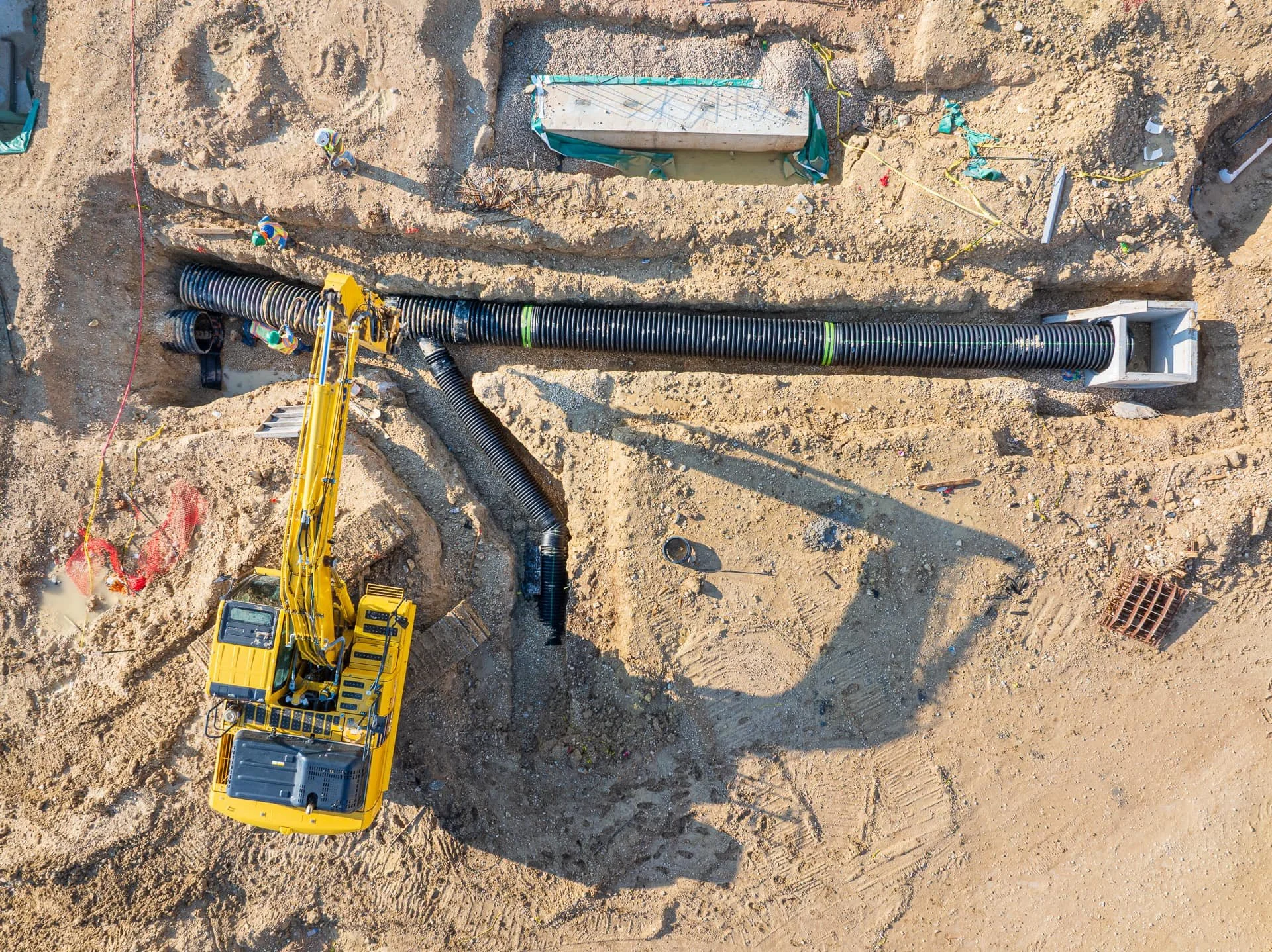 Excavator and crew installing drainage pipe system in trench for Section 01380 construction documentation in Austin, Texas.
