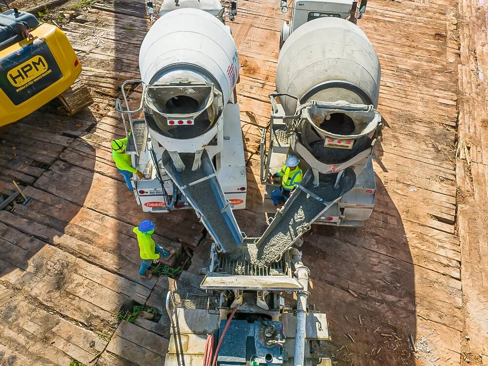 Aerial view of two concrete mixer trucks pouring into pump system with construction crew on site in Central Texas.