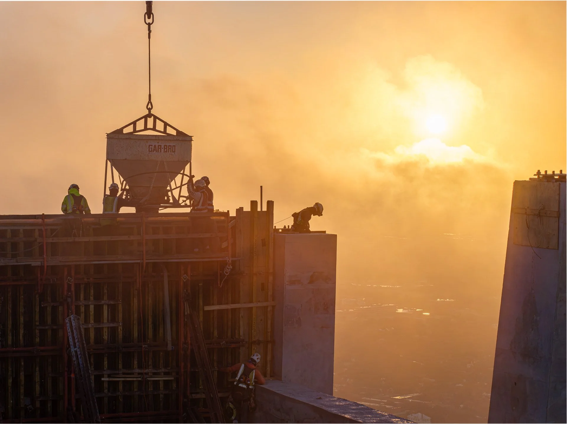 Construction crew guiding concrete bucket hoisted by crane during sunrise pour on high-rise in Austin, Texas.