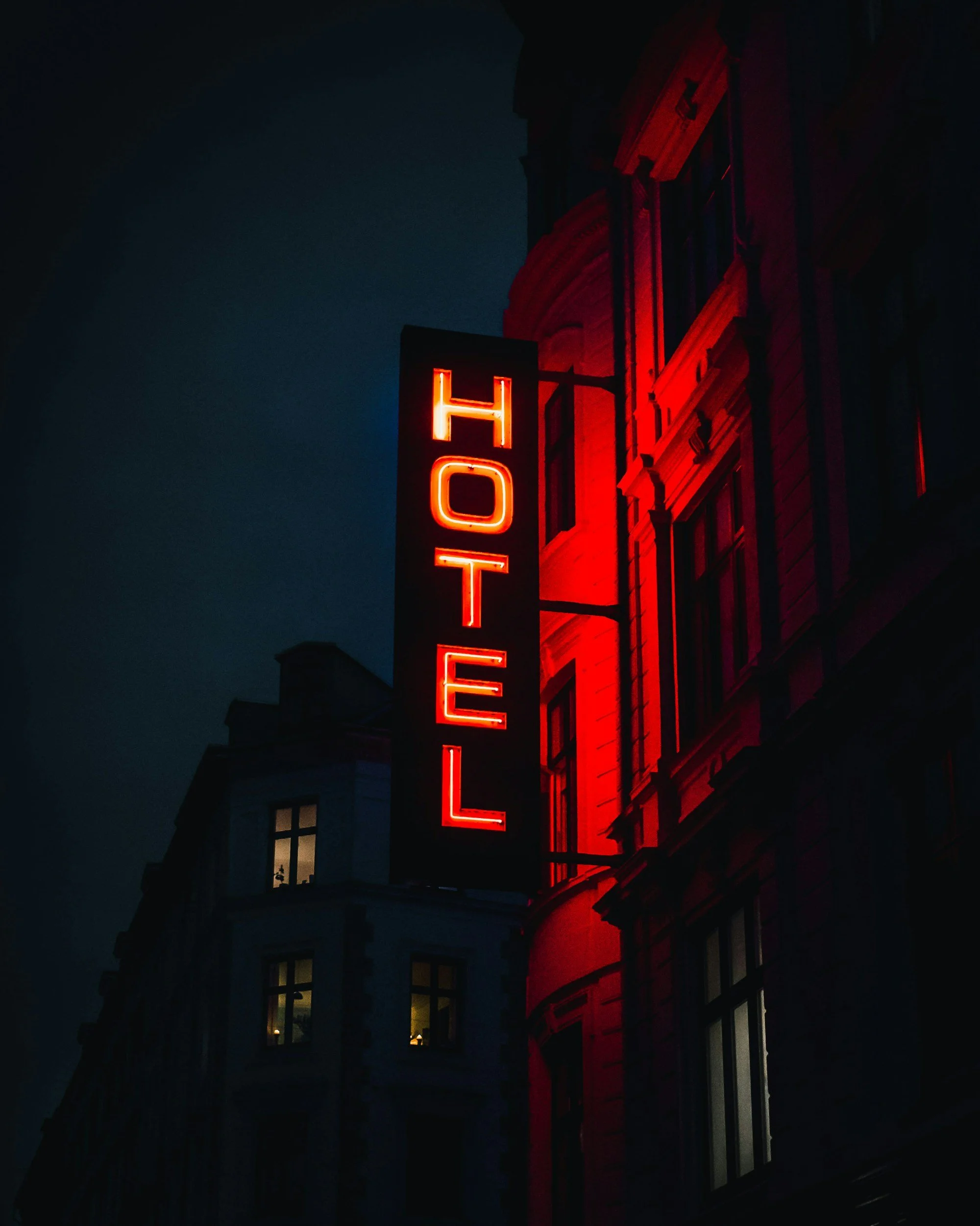 Nighttime view of a building with a vertically oriented red neon sign that reads 'HOTEL'.