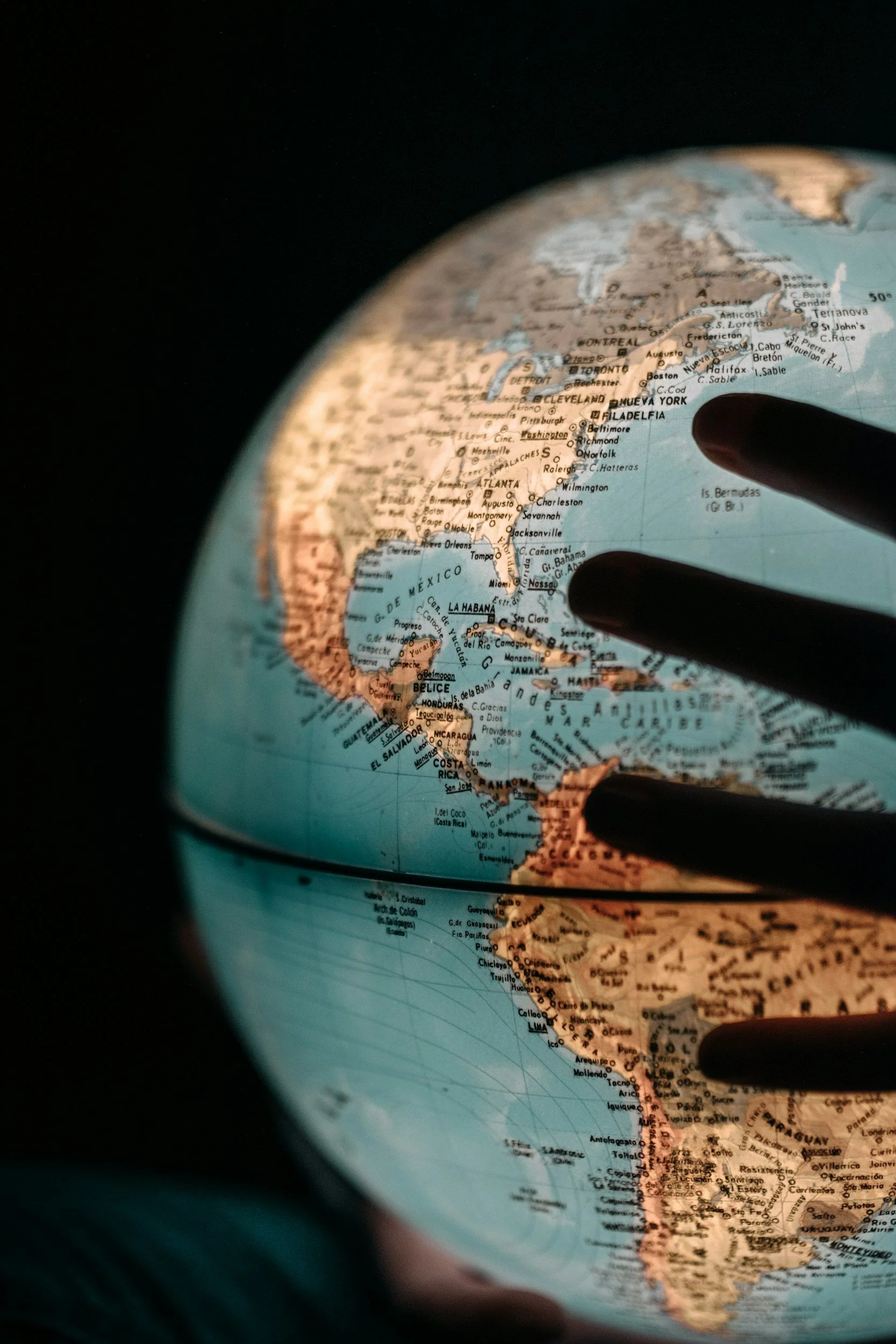 A globe showing North and South America, with a focus on the eastern coast of the United States and Mexico, and a person's fingers pointing at the map.