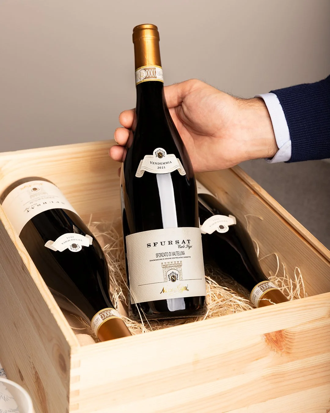 Person holding a bottle of wine in a wooden gift crate with two other bottles of wine inside.