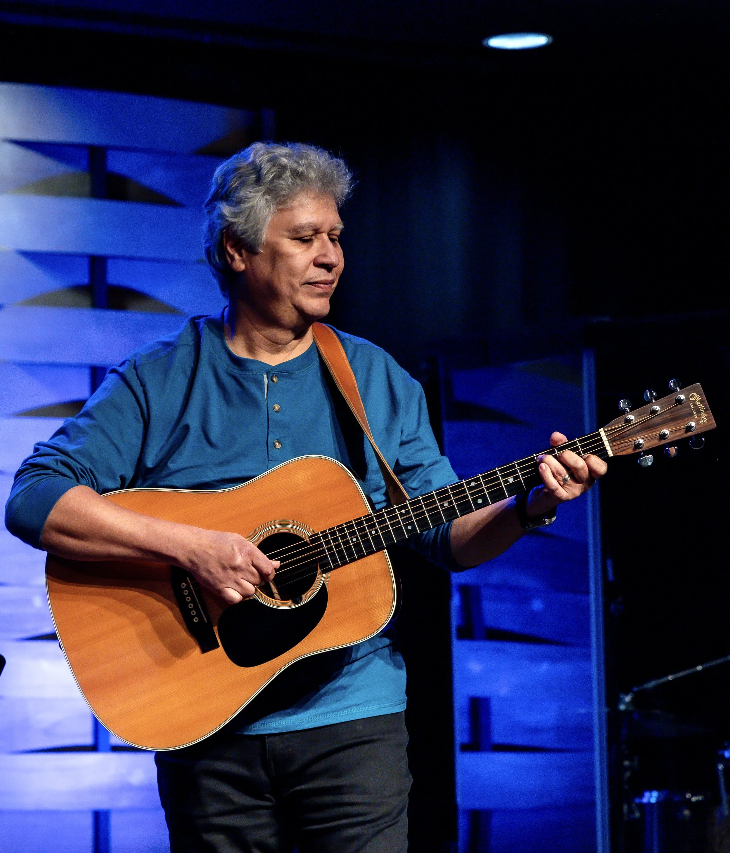 Marvin teaches guitar, bass, and mandolin at the Wylie School of Music. The photo shows him smiling as he plays the acoustic guitar at one of the music recitals in Wylie.