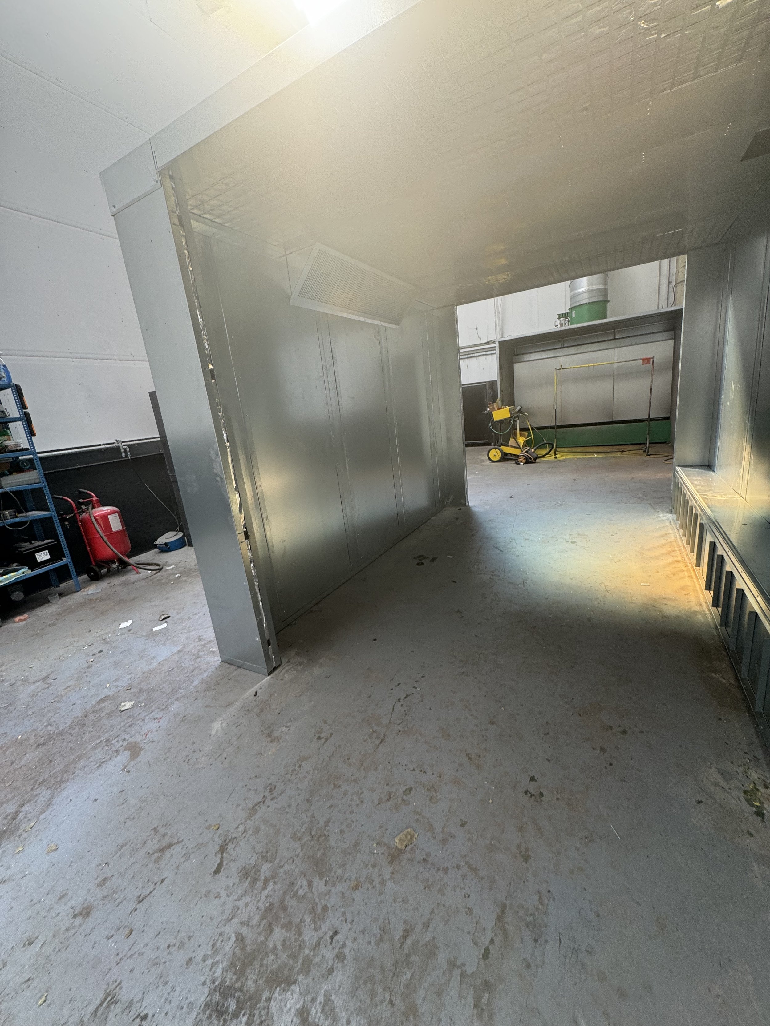 An unfinished industrial or commercial space with a concrete floor, metal walls and ceiling, and construction equipment and materials scattered around.