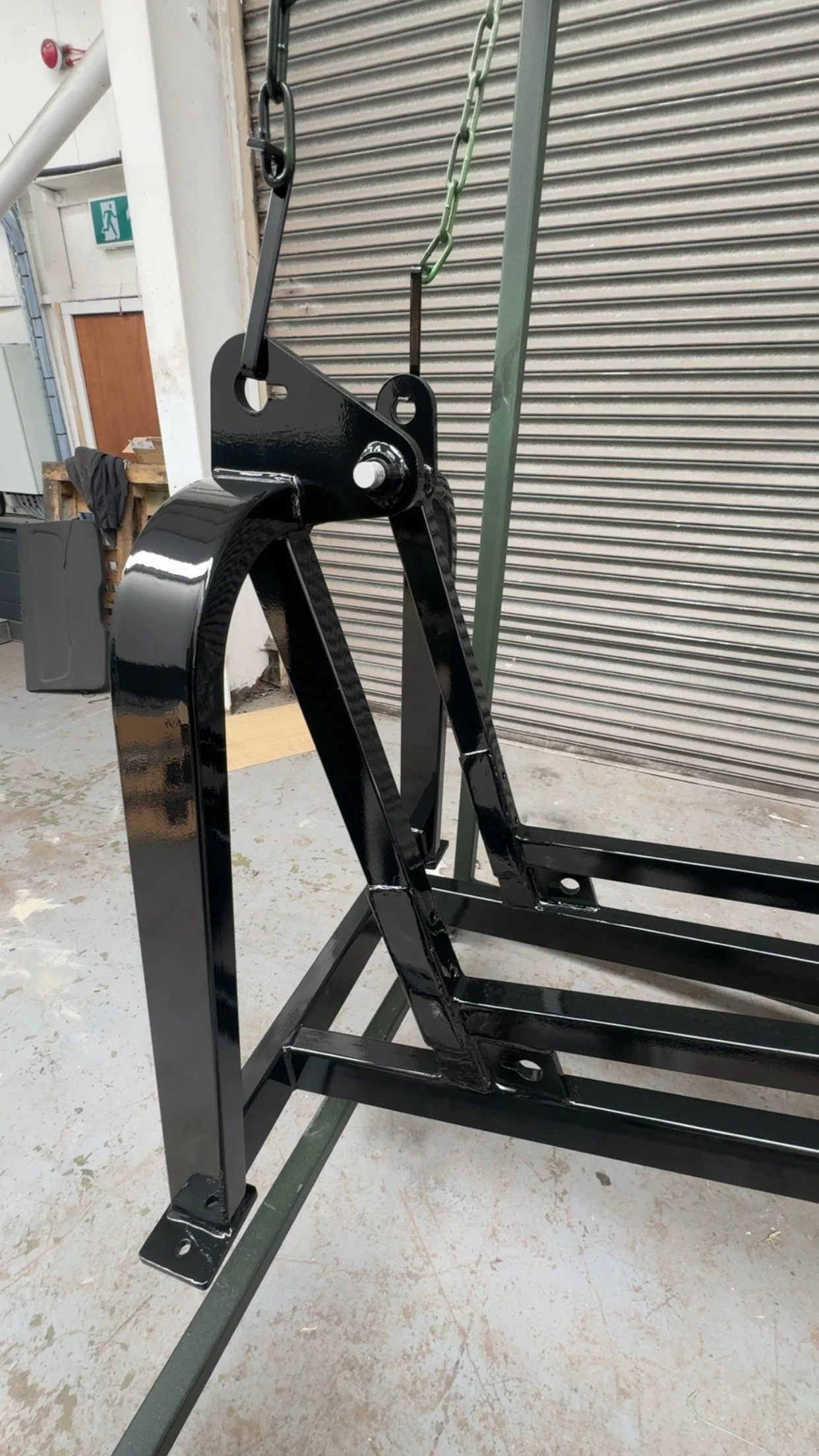 A black metal stand with chains hanging from it, situated indoors near a metal roll-up door and a wooden door.