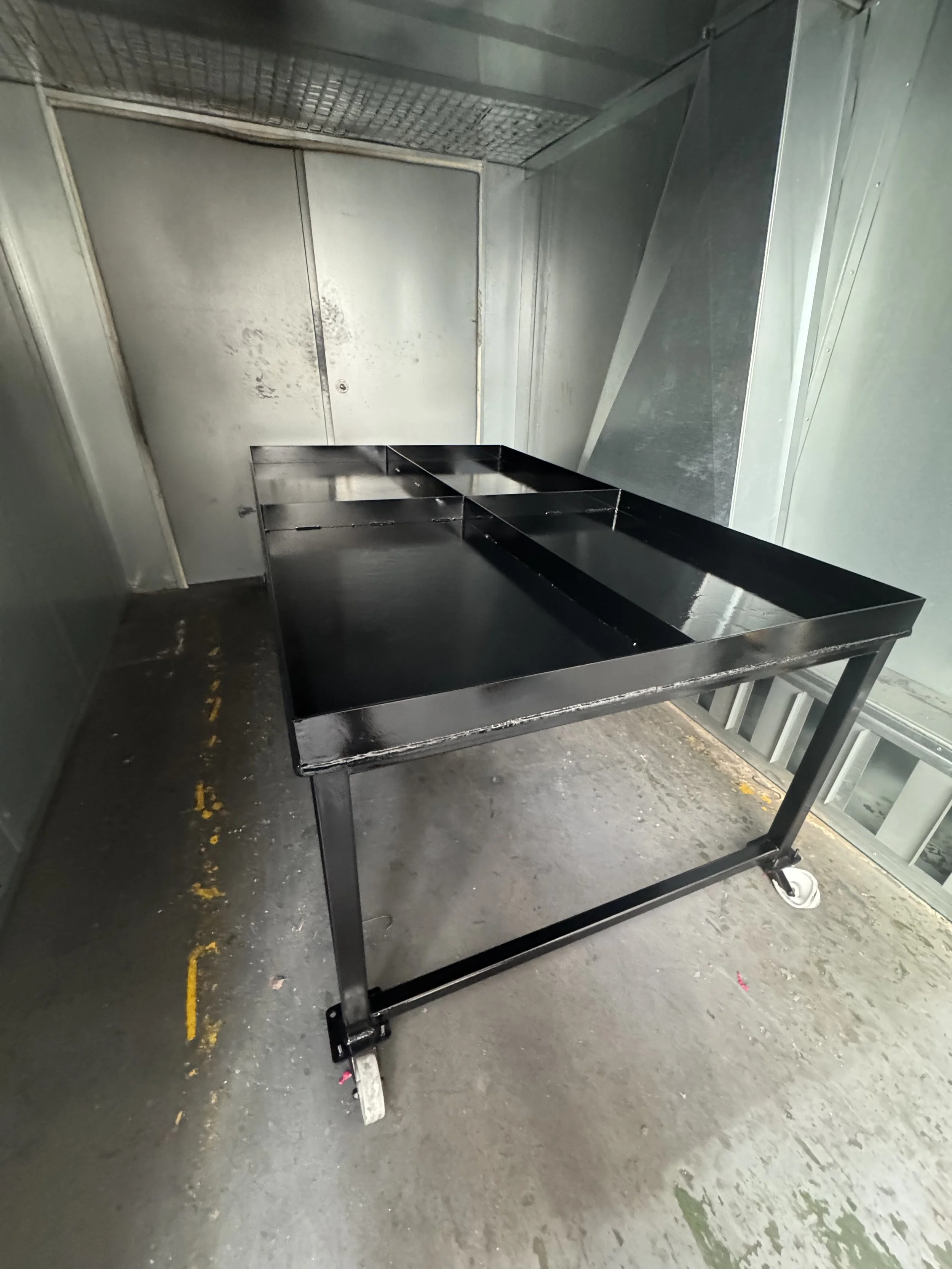Metal utility cart with multiple compartments in an industrial or storage room with concrete floors and metal walls.