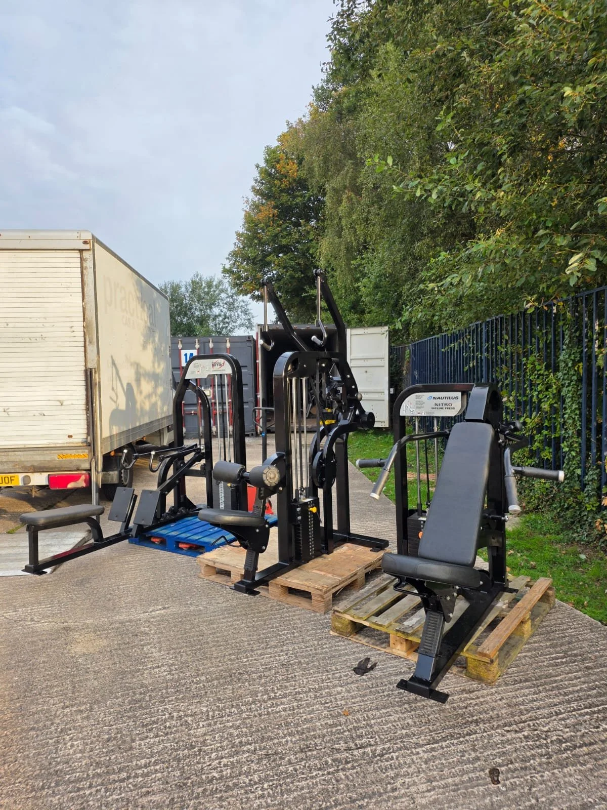 Outdoor gym equipment placed on wooden pallets, with trucks and trees in the background.