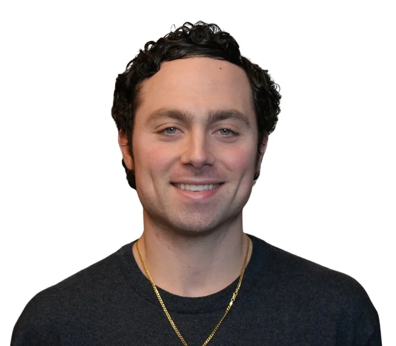 Smiling man wearing a black t-shirt and gold necklace against white background.