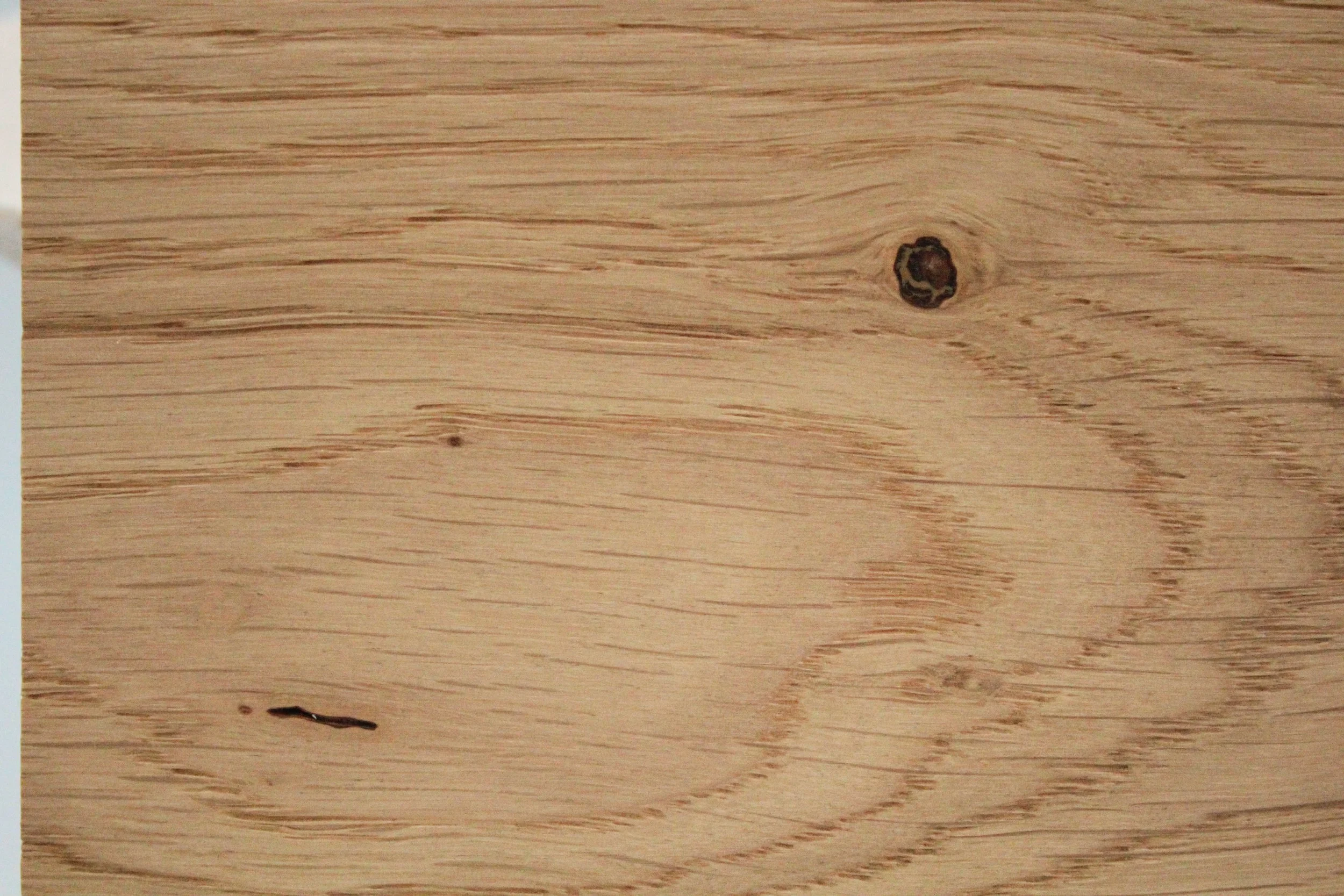 Close-up of light-colored wooden surface showing wood grain patterns and knots.