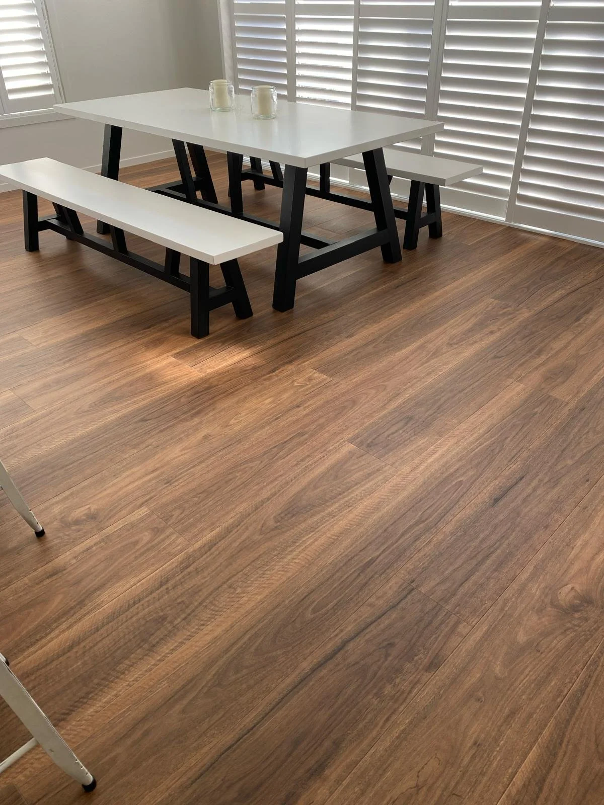 A dining area with a black and white table, black benches, candles, and white shutters on windows.