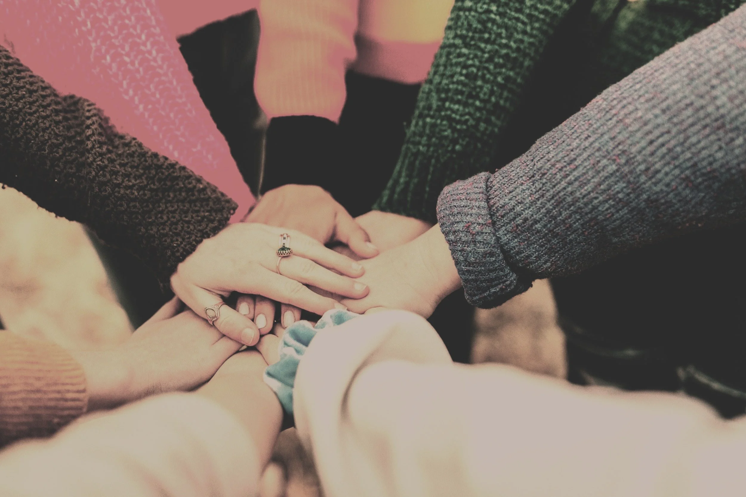 Multiple people stacking their hands together in the center, symbolizing unity and teamwork.