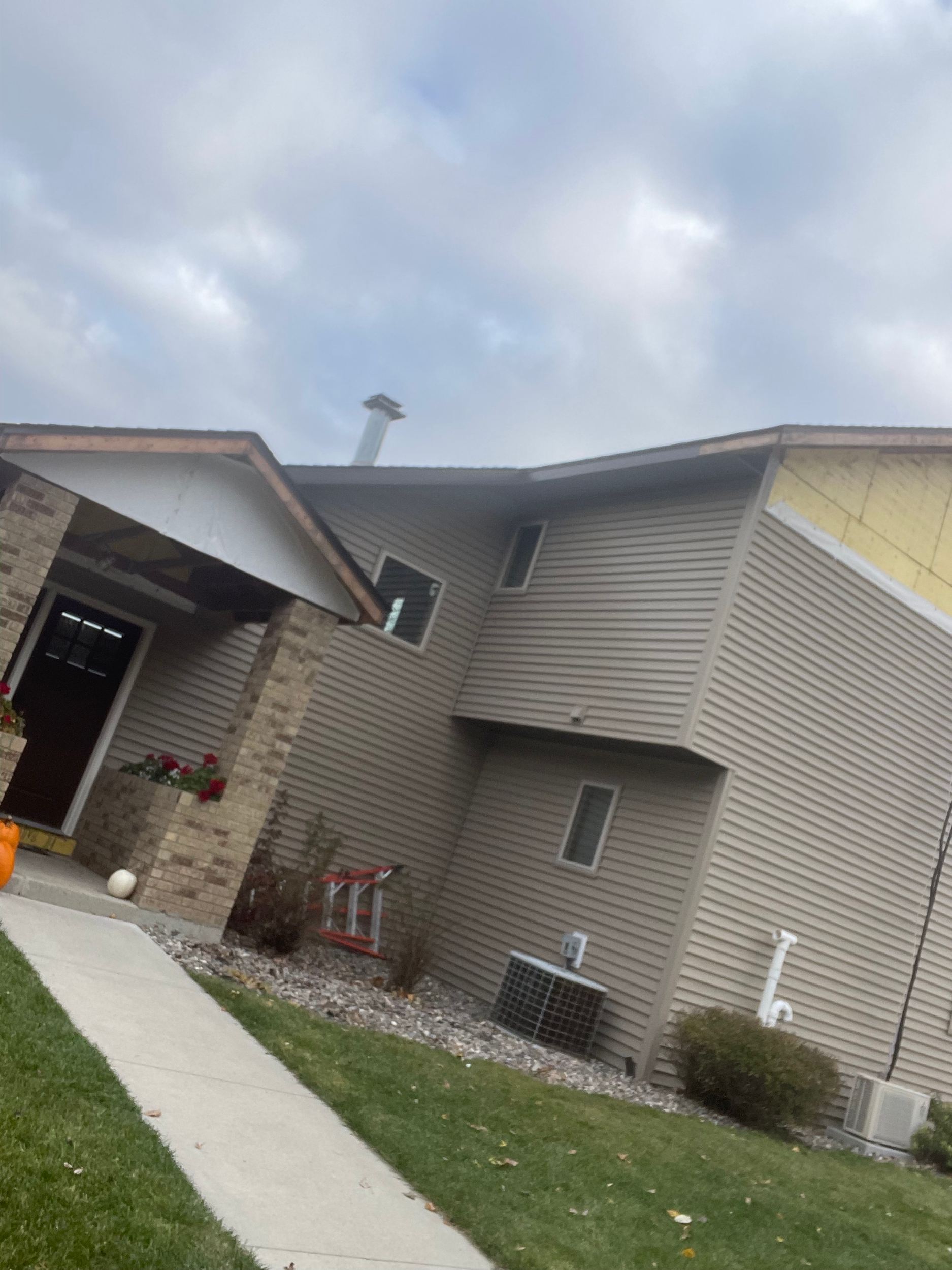 Backyard of a house with beige siding, a small porch, a potted plant with red flowers, a small fence, and a patch of grass with a sidewalk.
